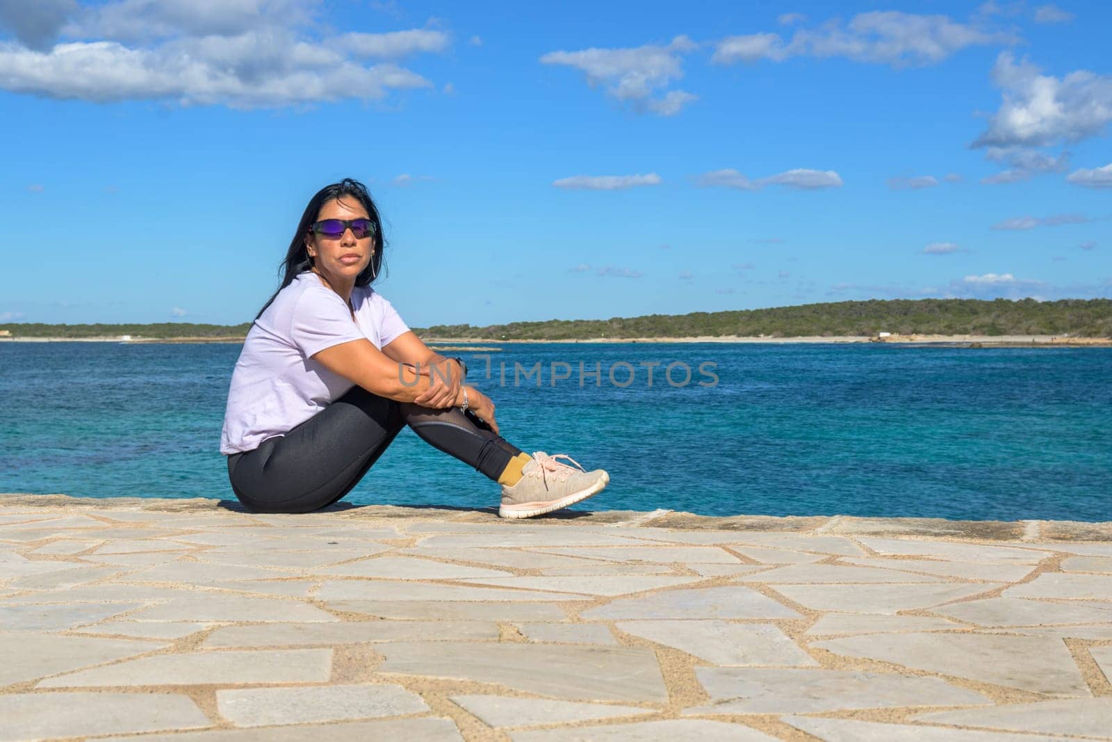 Woman sitting by the ocean, appearing serene, beautiful latina woman by the sea in Colonia San Jordi, Balearic Islands, Majorca, Spain