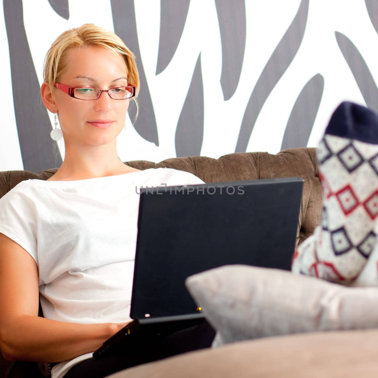 Relaxed, beautiful young woman sitting on sofa, using laptop computer, working from home.