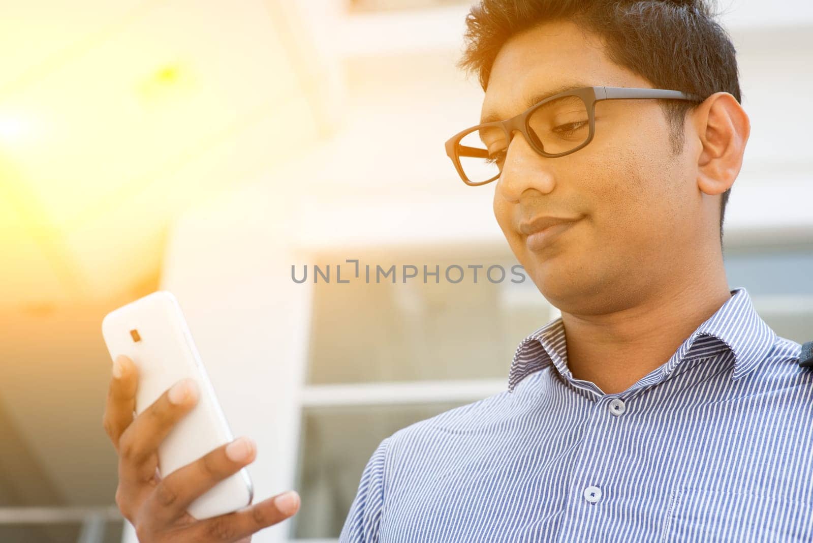 Asian Indian business people using smartphone, modern urban sunrise view.