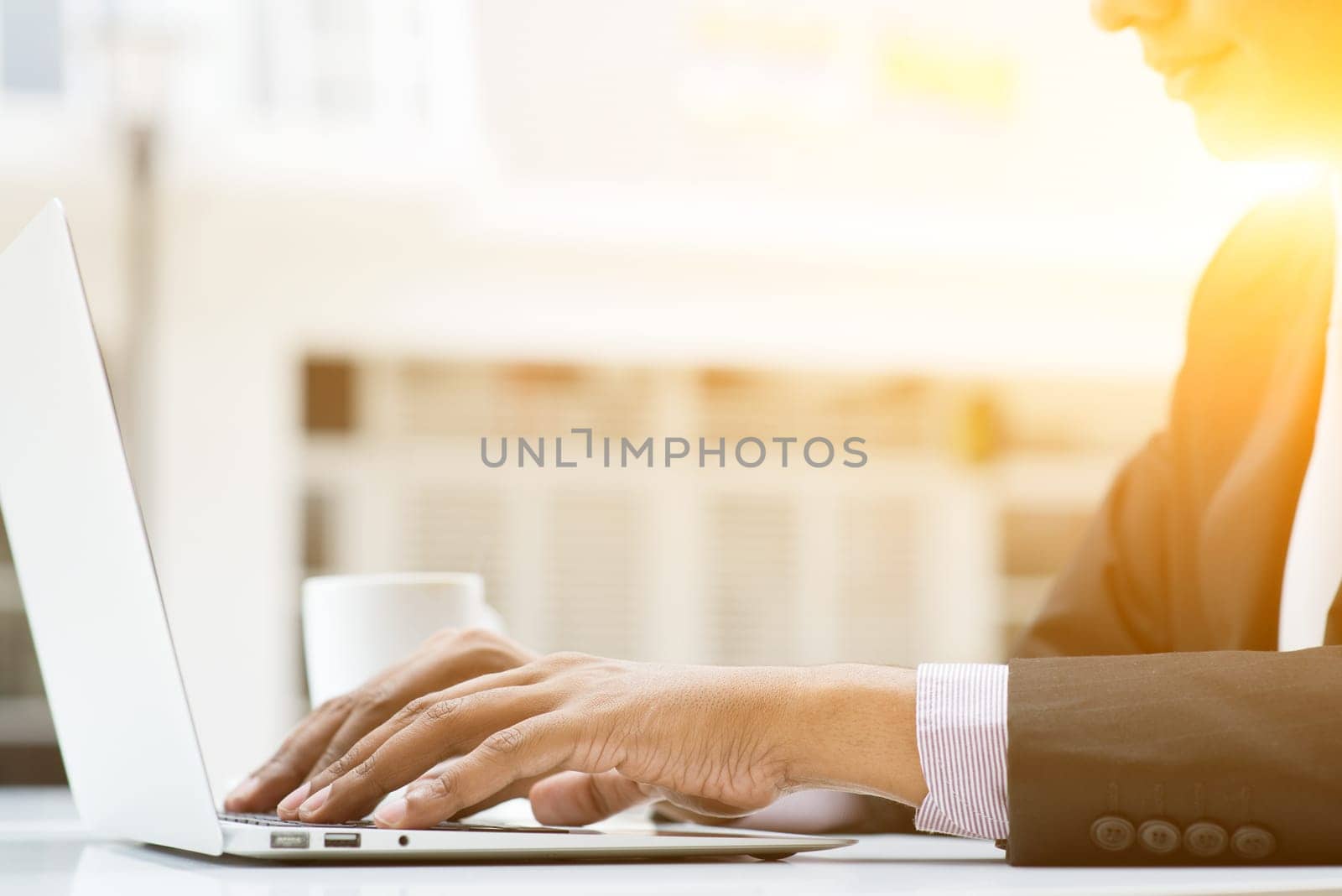 Business people using a laptop or notebook computer at cafe, with a cup of coffee. Male business man, modern building with beautiful golden sunlight as background.