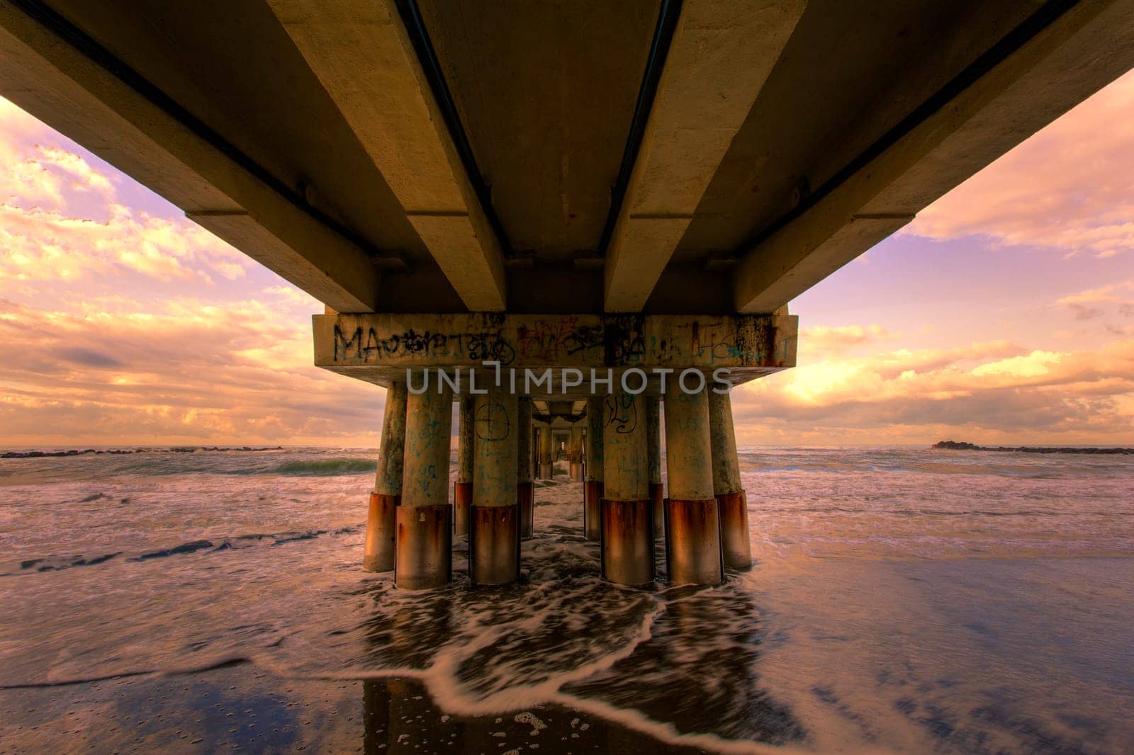 View of seascape from under a piermarine pillars lit by morning sun