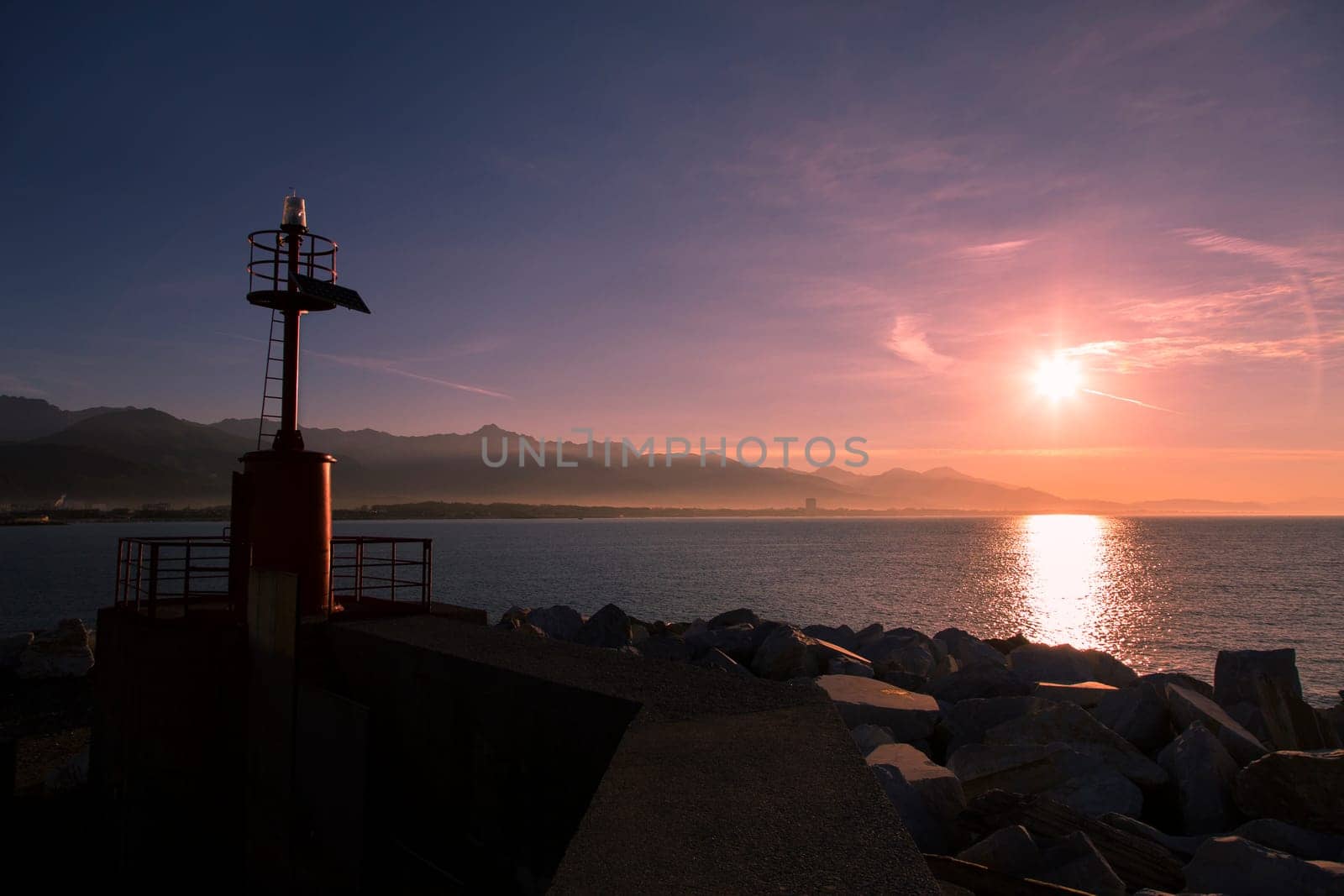 Costal landscape with lighthouse in backlight and the mountain range in the background