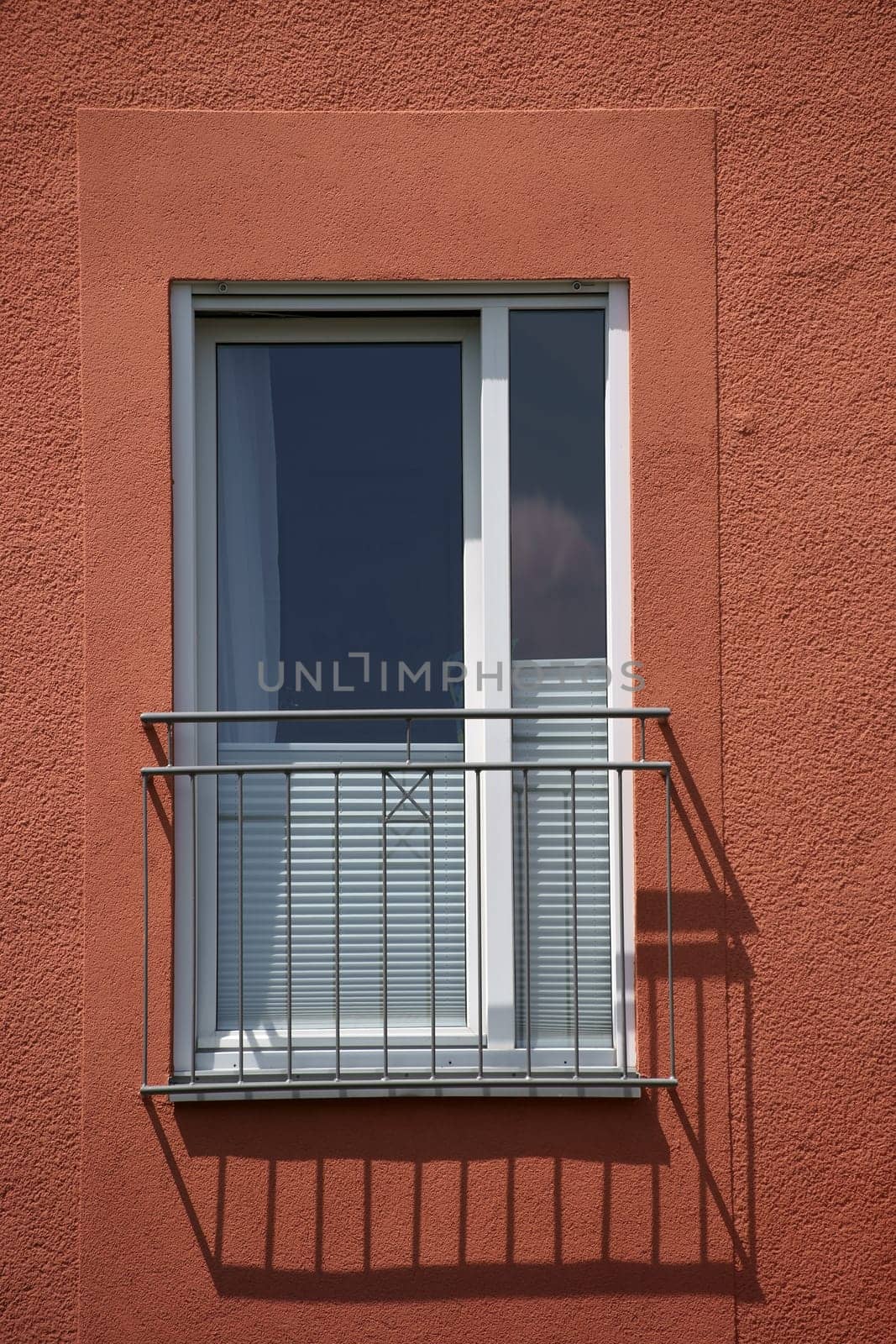 A railing in front of a window of a residential building casts a shadow.