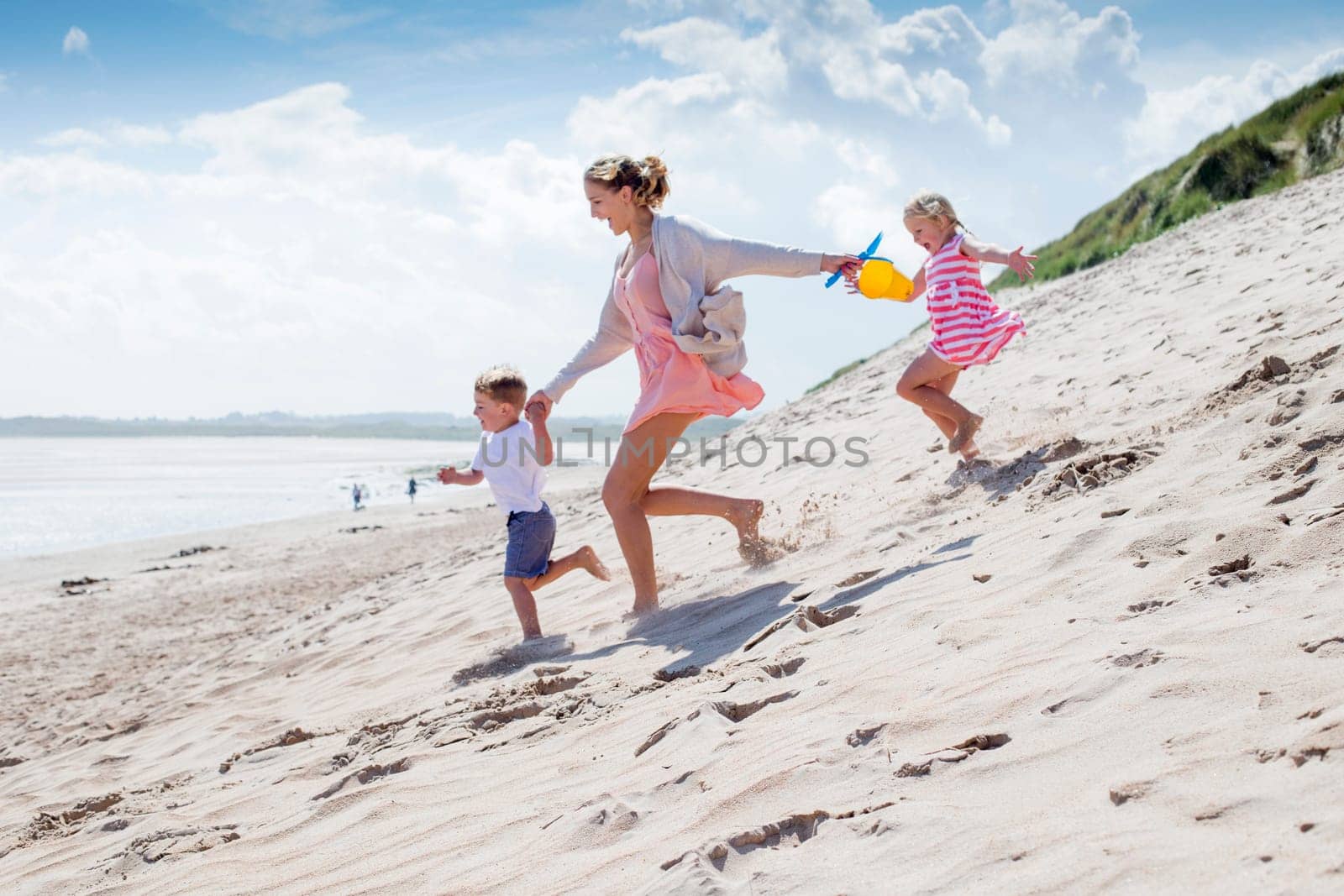 Young single parent family holding hands and running down the sanddunes to the sea. They are laughing and wearing casual clothing.