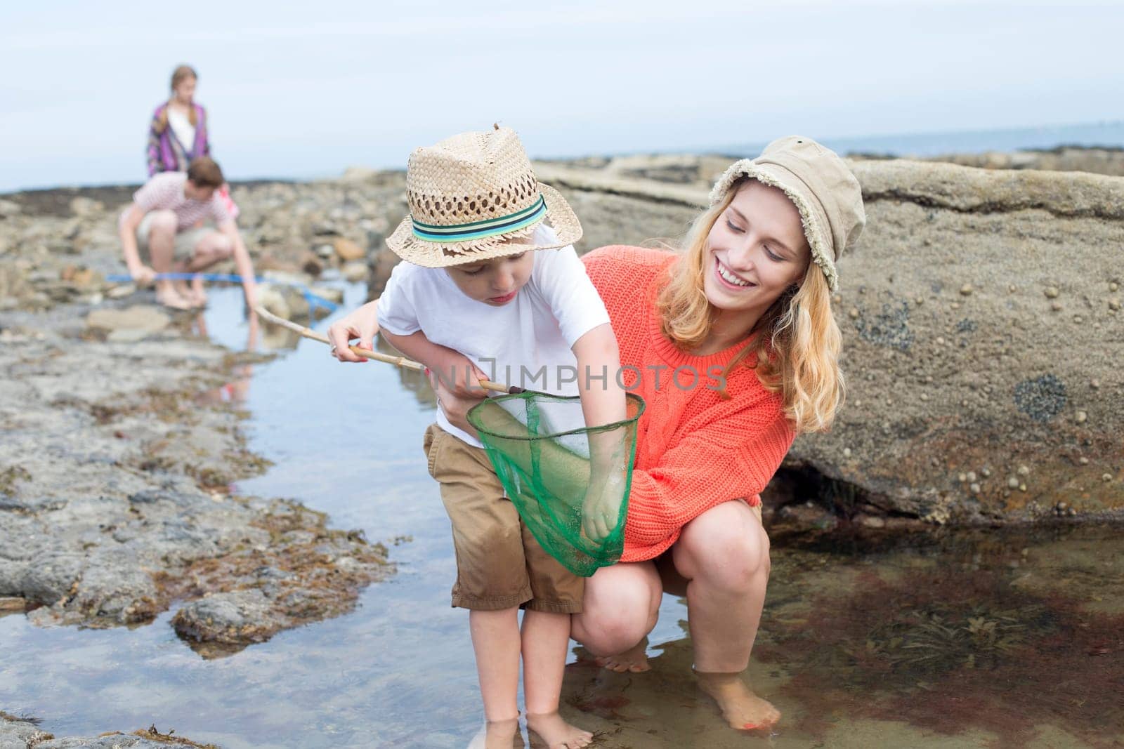 Young family searching for crabs among the rocks at the seaside. The young boy is reaching into his net for a crab and his mother is looking at him and smiling.