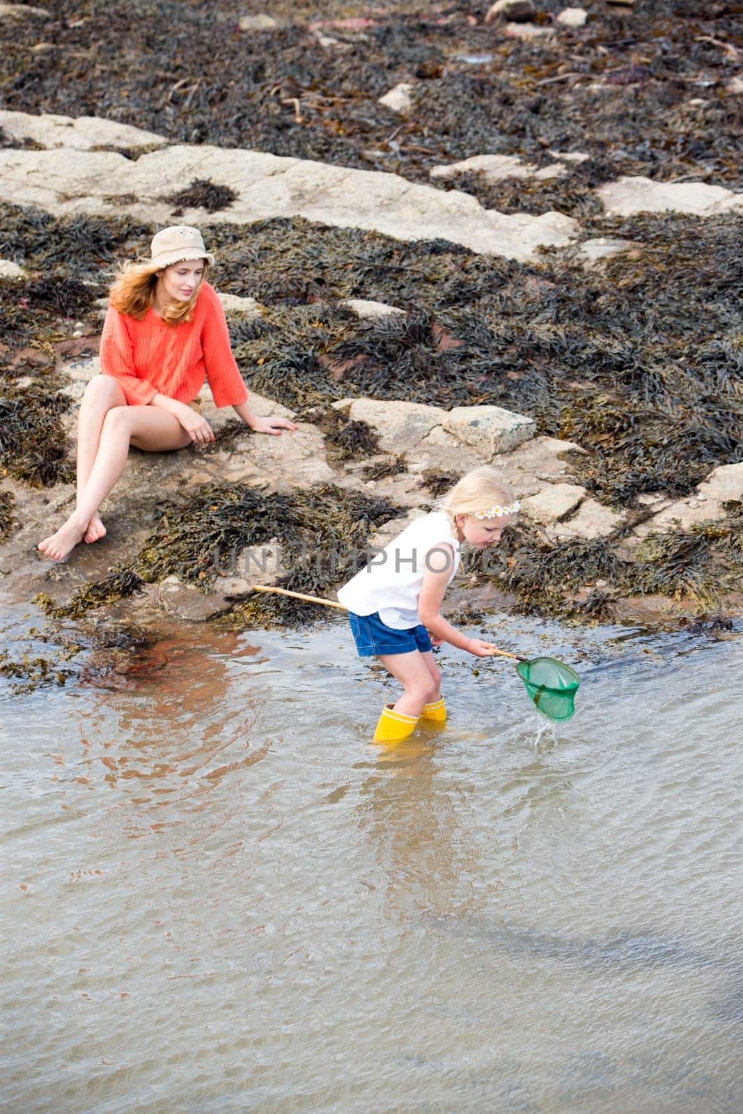 Young mother and her daughter searching for fish and crabs at the seaside. The young girl is holding her net and standing in the water.