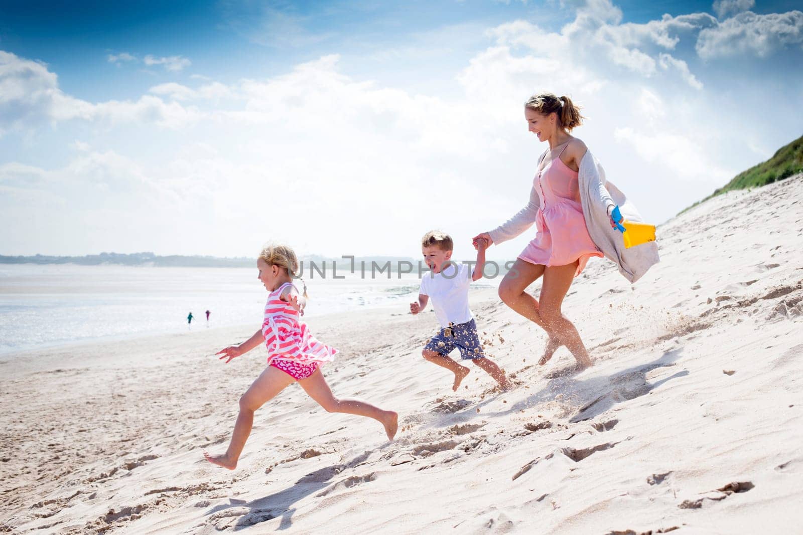 Young single parent family running down the sanddunes at the beach.