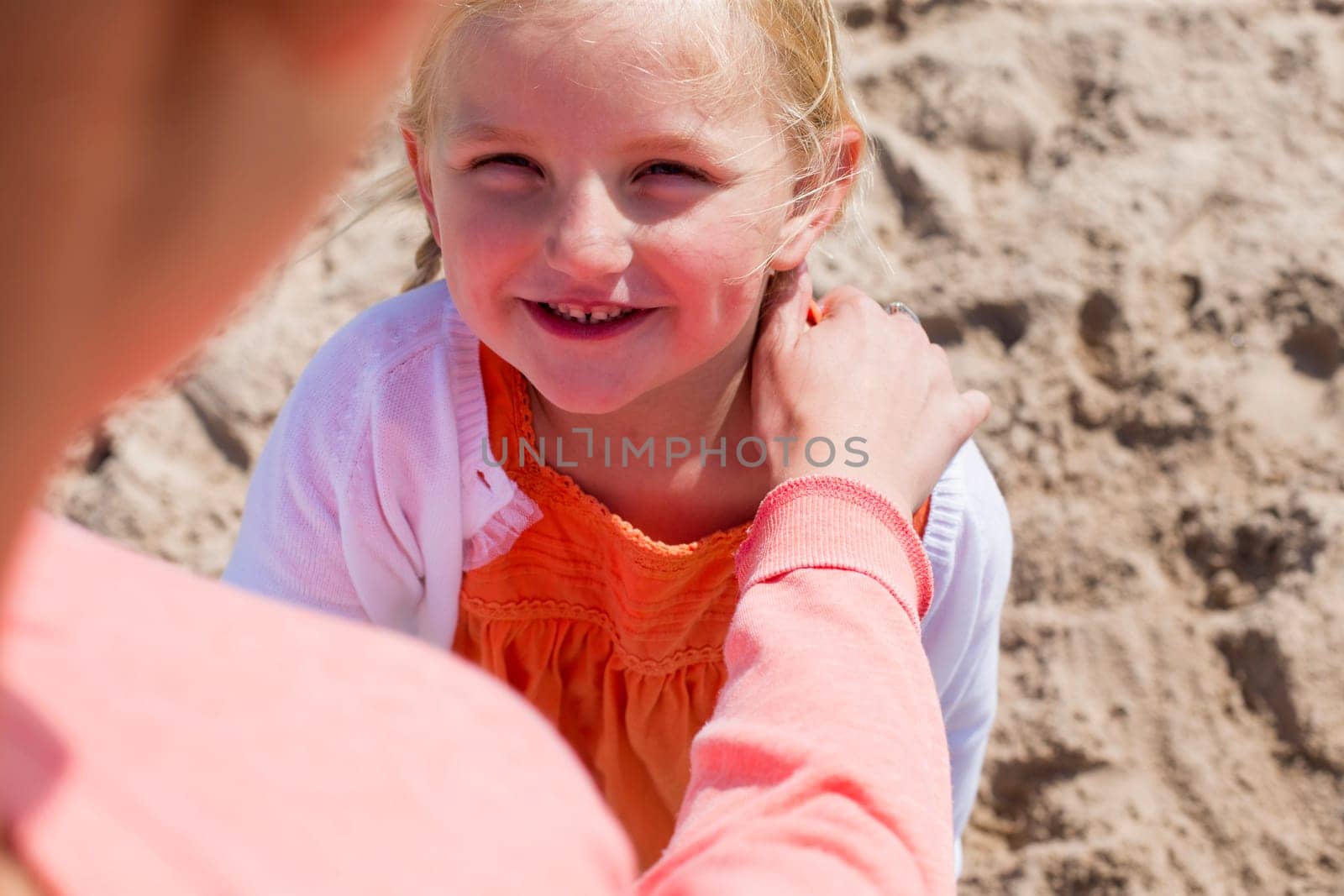 Young girl at the beach looking up at her mother and smiling.