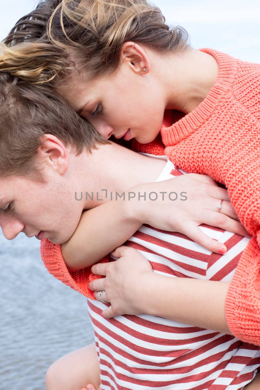 Close up of a beautiful young couple at the beach. They are wearing casual clothing and are cuddled in together.