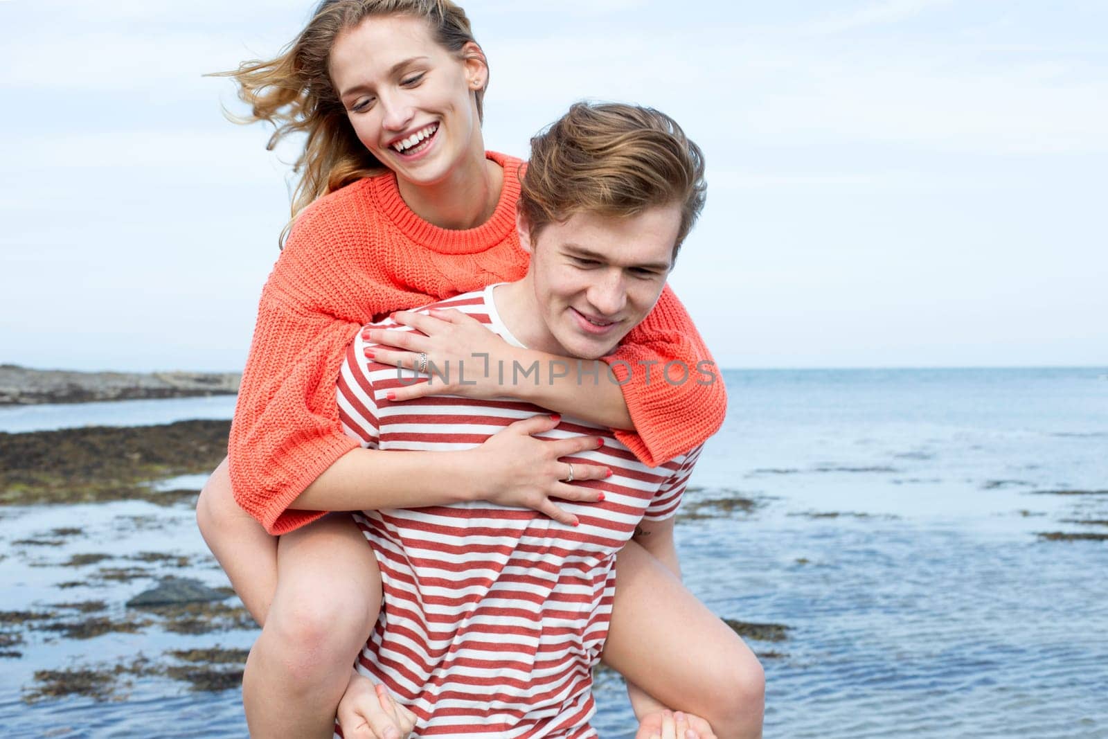 Beautiful young couple at the beach. They are smiling and the young woman is having a piggyback from her boyfriend.