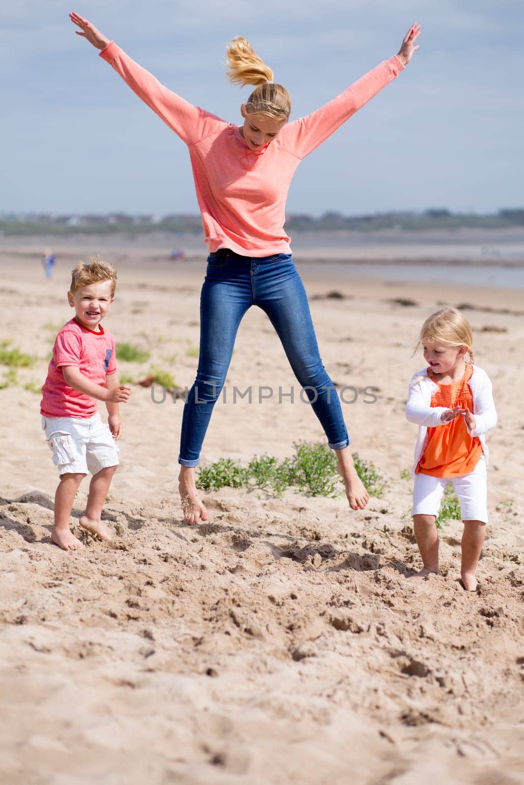 Beautiful little family playing together at the beach. The mother is jumping in the air while her children play around her.