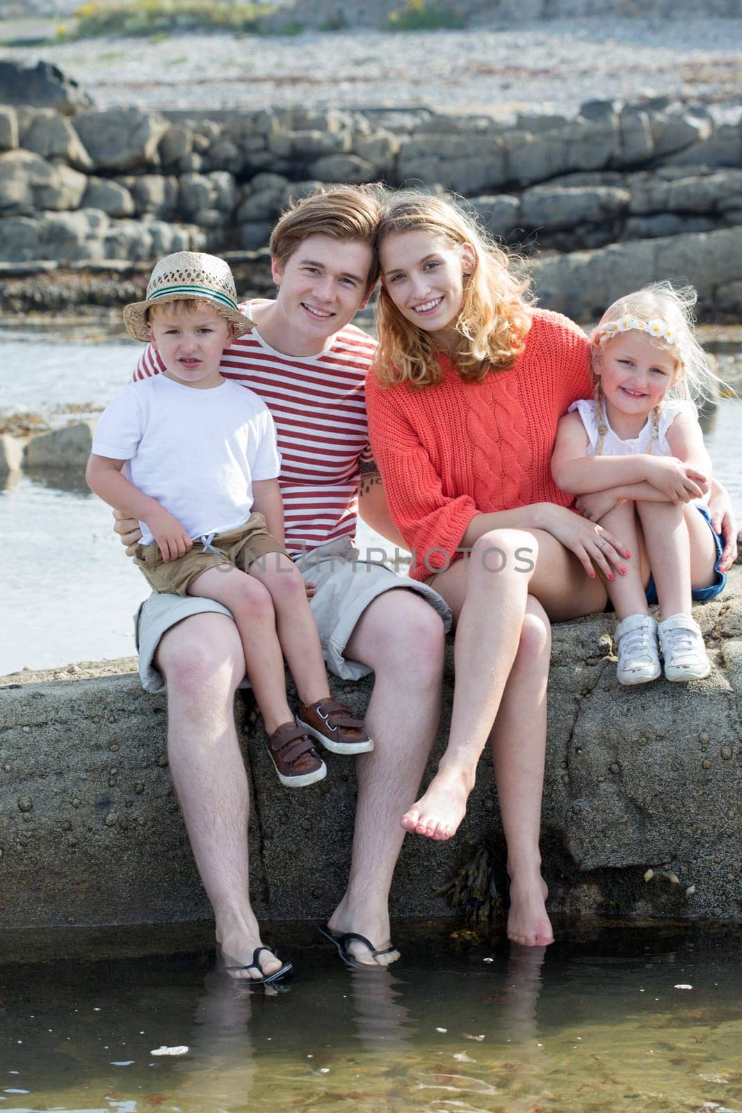 Portrait of a beautiful young family at the beach. They are wearing casual clothing and smiling at the camera.