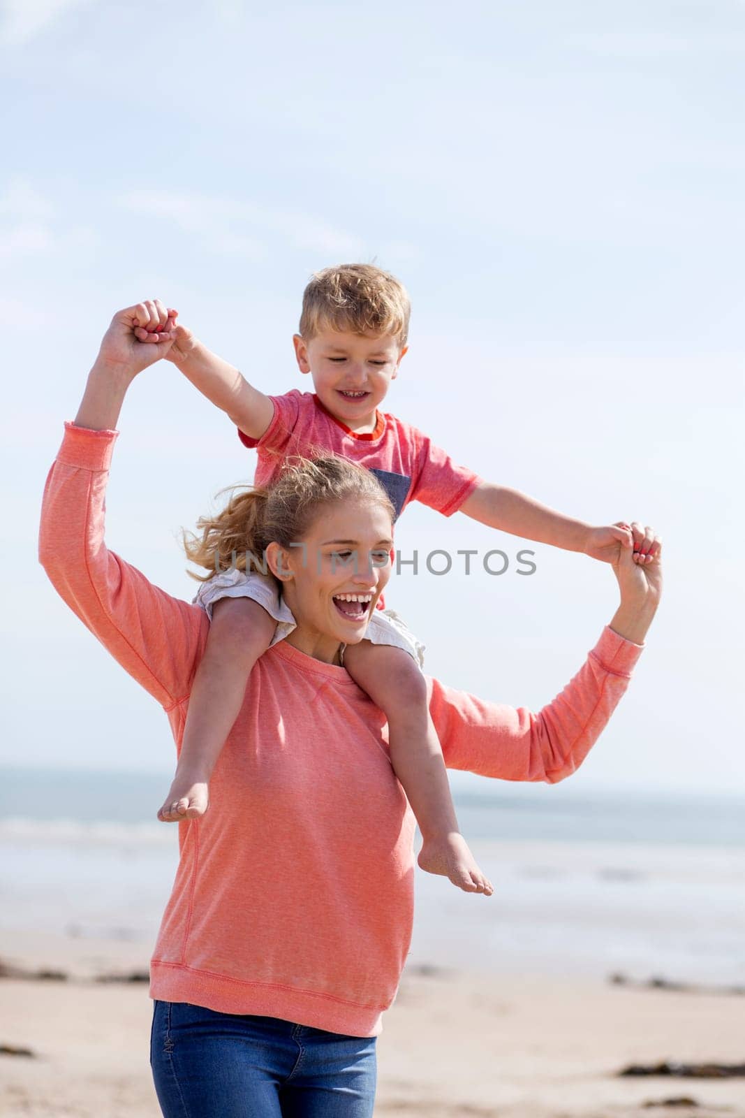 Portrait of a young mother and son at the beach together. They are both smiling and the little boy is on his mothers shoulders.