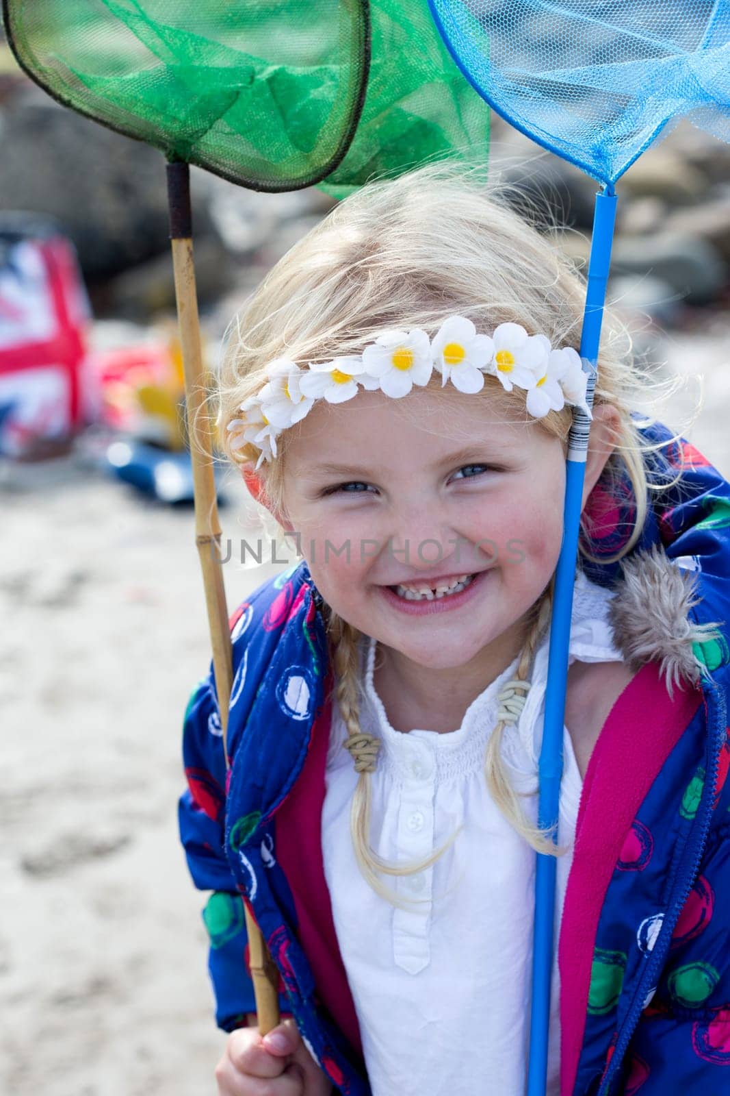 Portrait of a little girl at the beach holding fishing rods. She is wearing casual clothing and smiling at the camera.