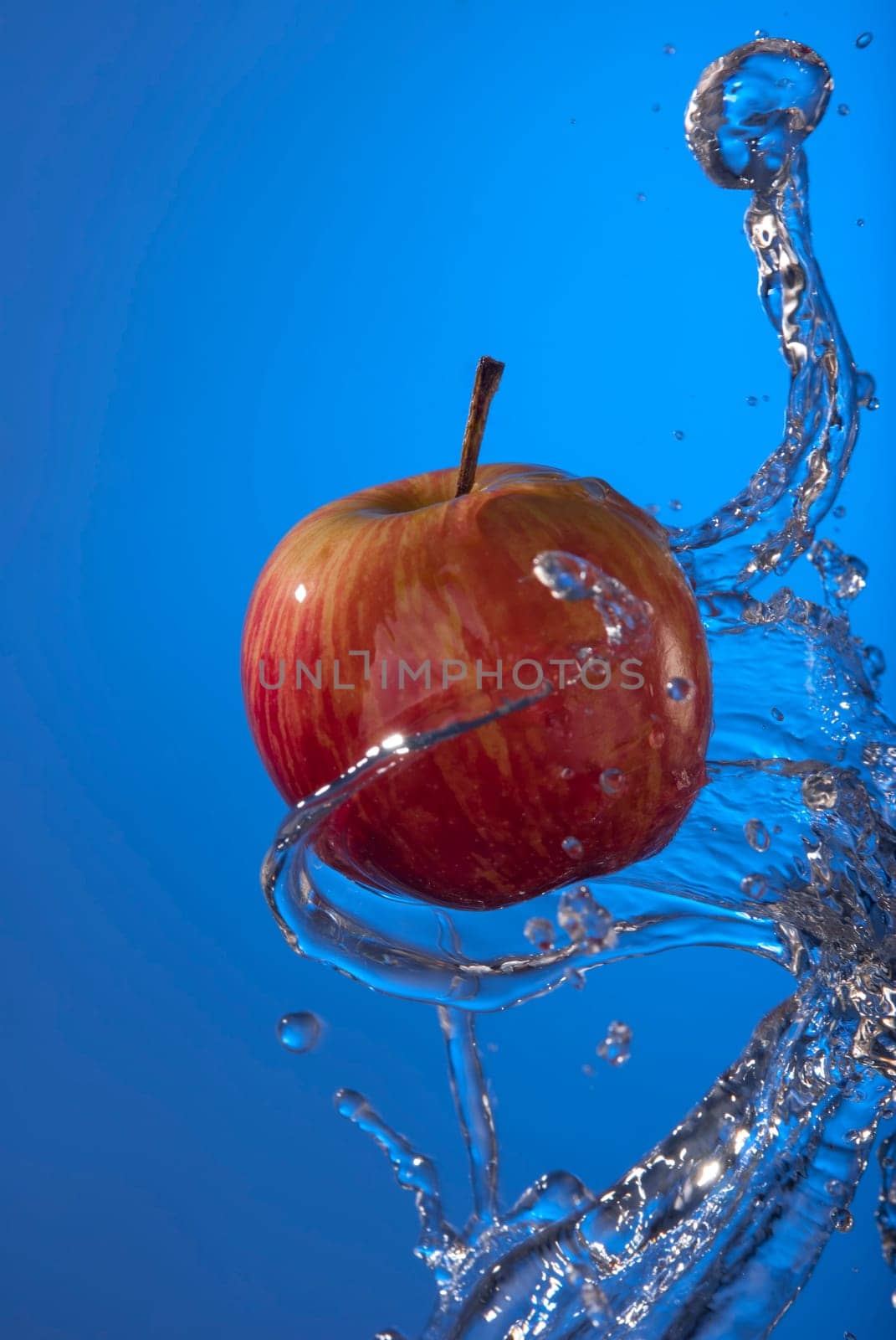 Organic eco red apple fruit with water splash on blue background. Ideal for poster or health campaign.