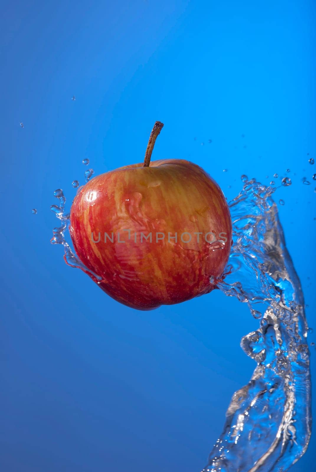 Delicious organic red apple fruit on blue background with water splash motion. Ideal for health campaign or poster.