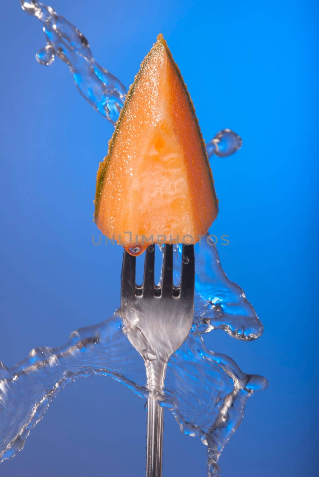 Melon fruit piece on fork with water splash and empty blue background concept photo. Ideal for healthy eating campaign, motivation or fitness poster.   .