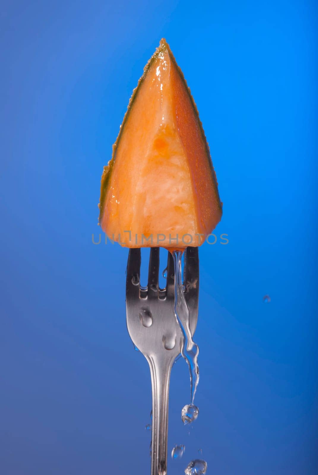 Melon fruit piece on fork with water splash and empty blue background concept photo. Ideal for healthy eating campaign, motivation or fitness poster.   .