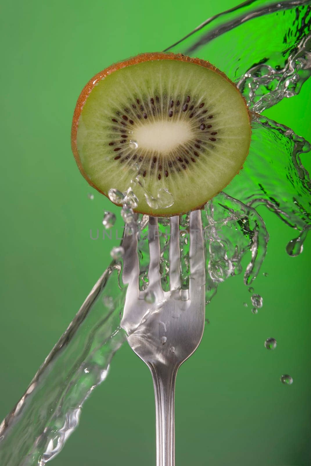 Kiwi fruit on fork with water splash and color background, concept photo. Ideal for healthy eating campaign or fitness poster.