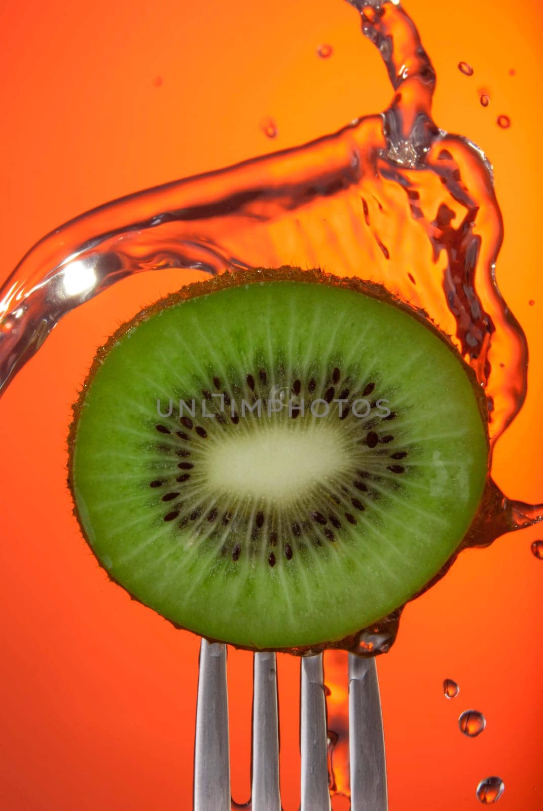 Close up of kiwi fruit center on fork with water splash and color background, concept photo. Ideal for healthy eating campaign or fitness poster.