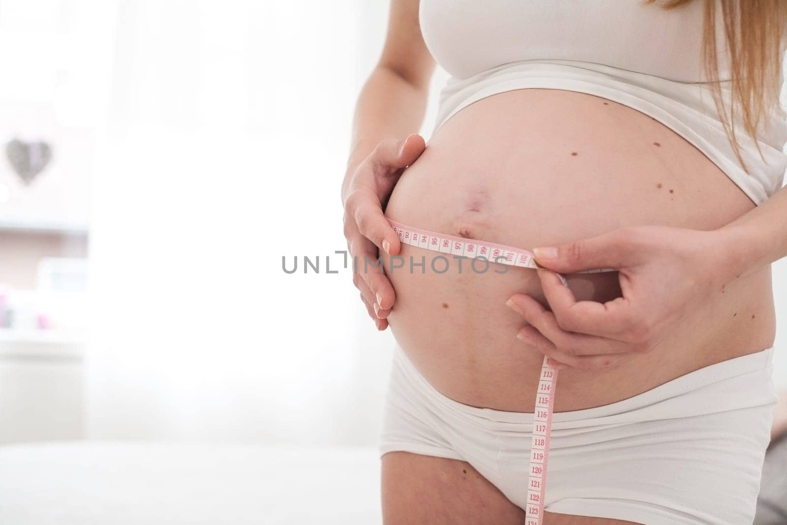 Young new mother is measuring her size of her belly