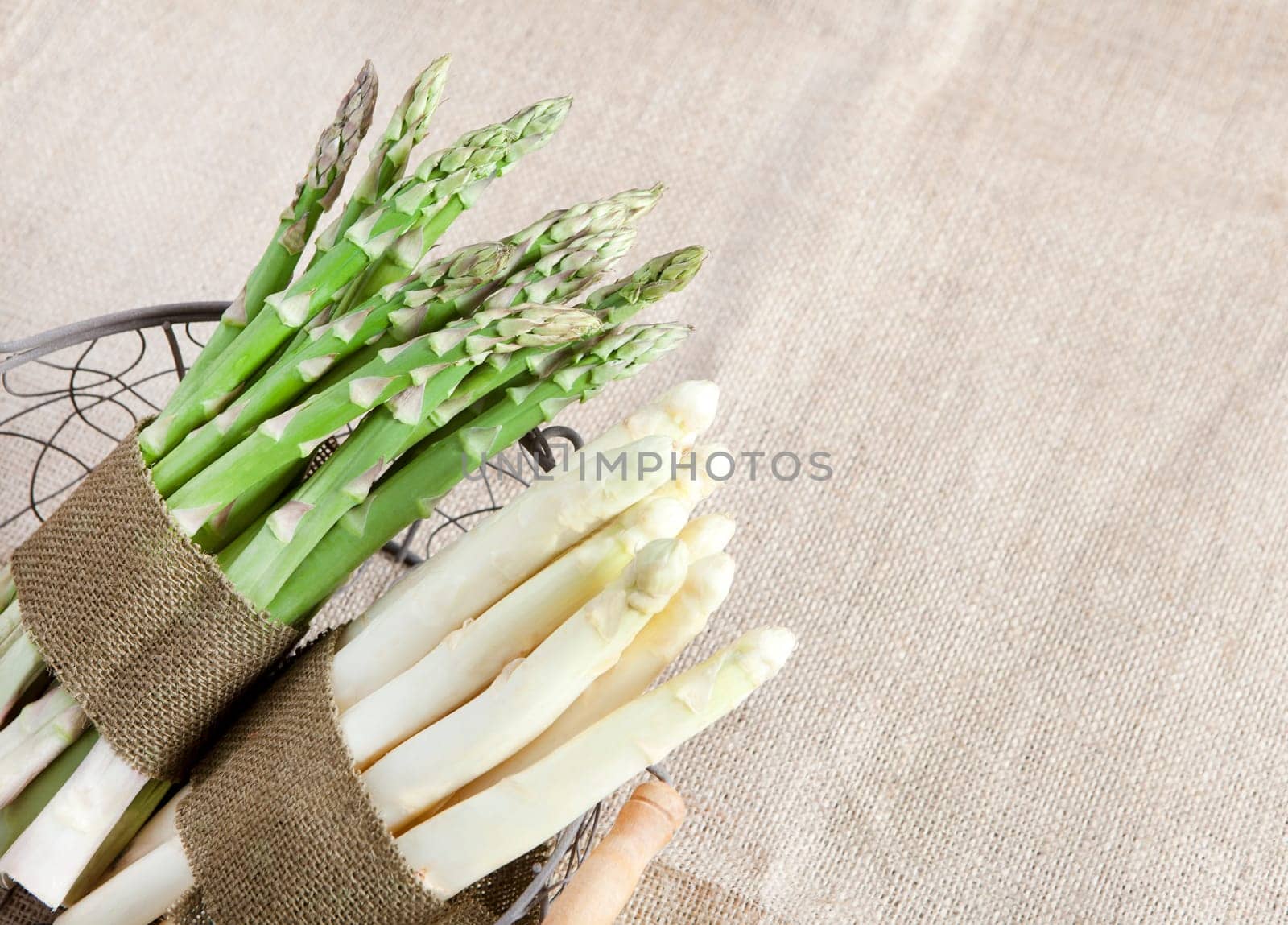 fresh green and white asparagus bundled in a basket with a cloth ribbon