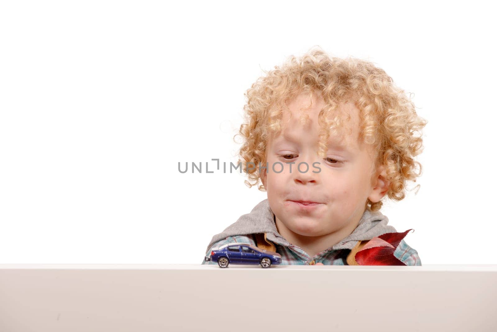 A portrait of a little blond boy looking at a toy car on white background