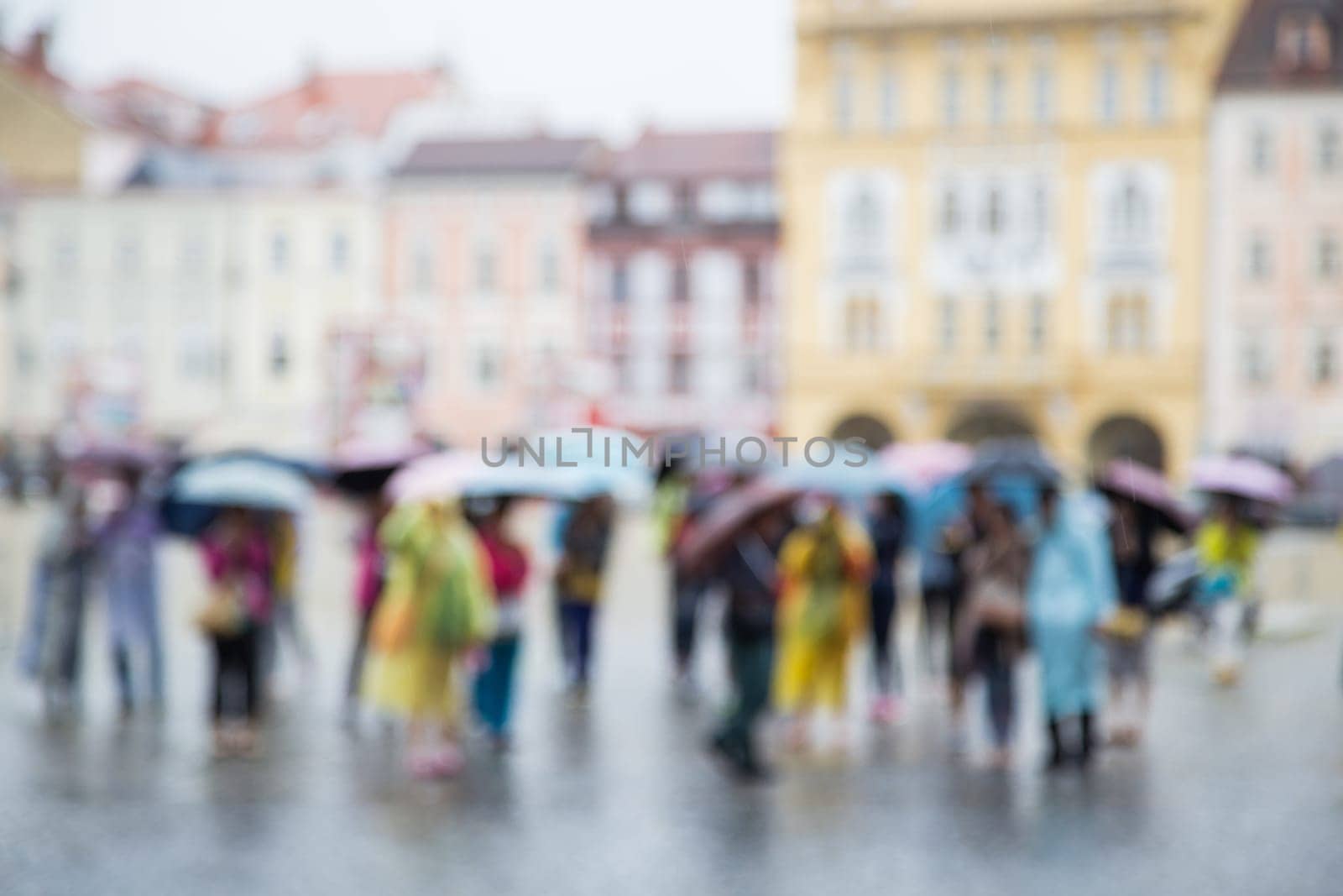 Out of focus shot of a group of people standing with umbrellas in the rain, buildings in the background