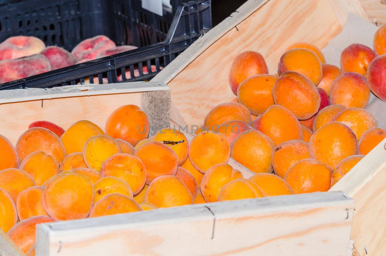 Fresh peaches in a wooden box for sale at a farmers market.