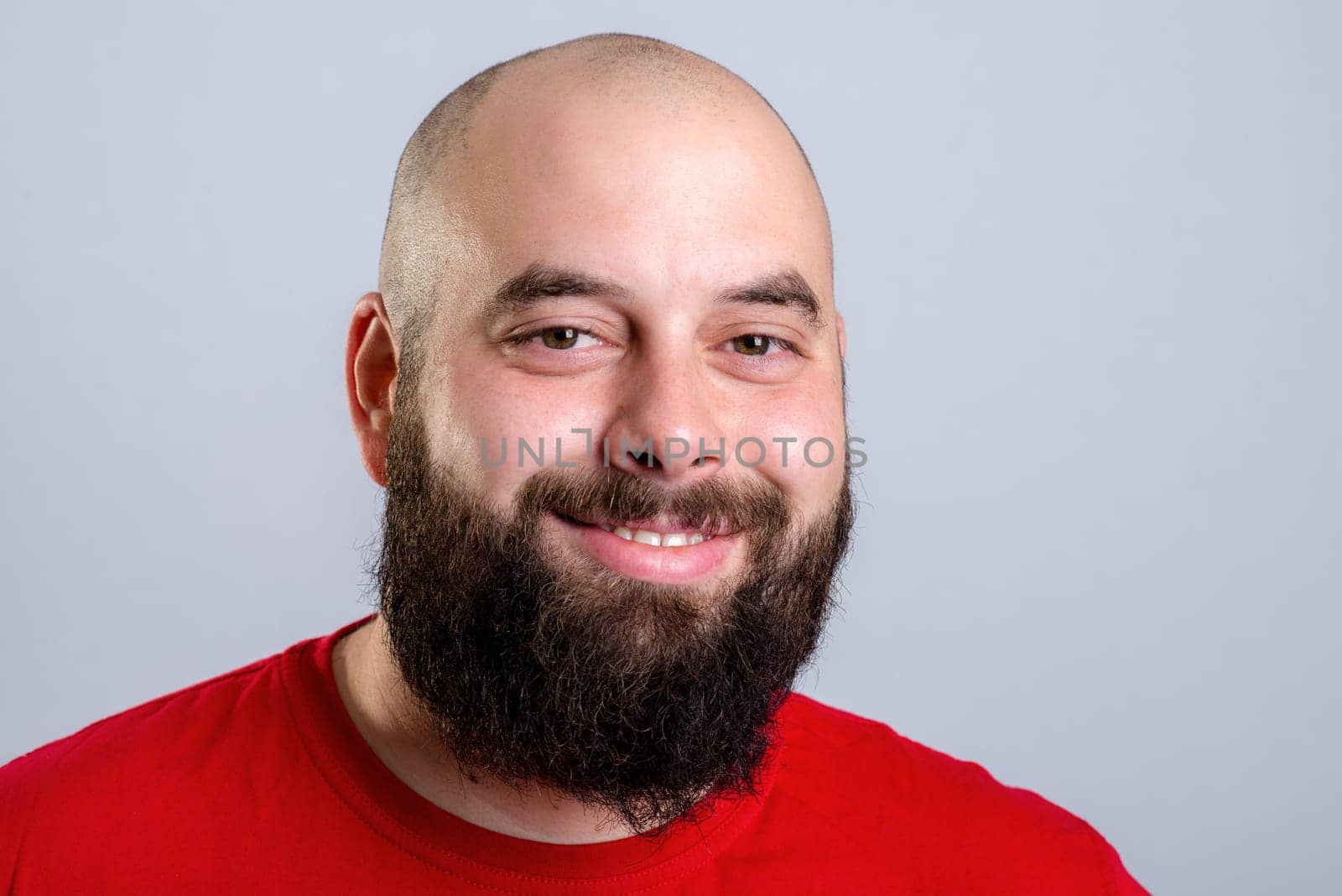 young bearded man in red shirt in front of gray background