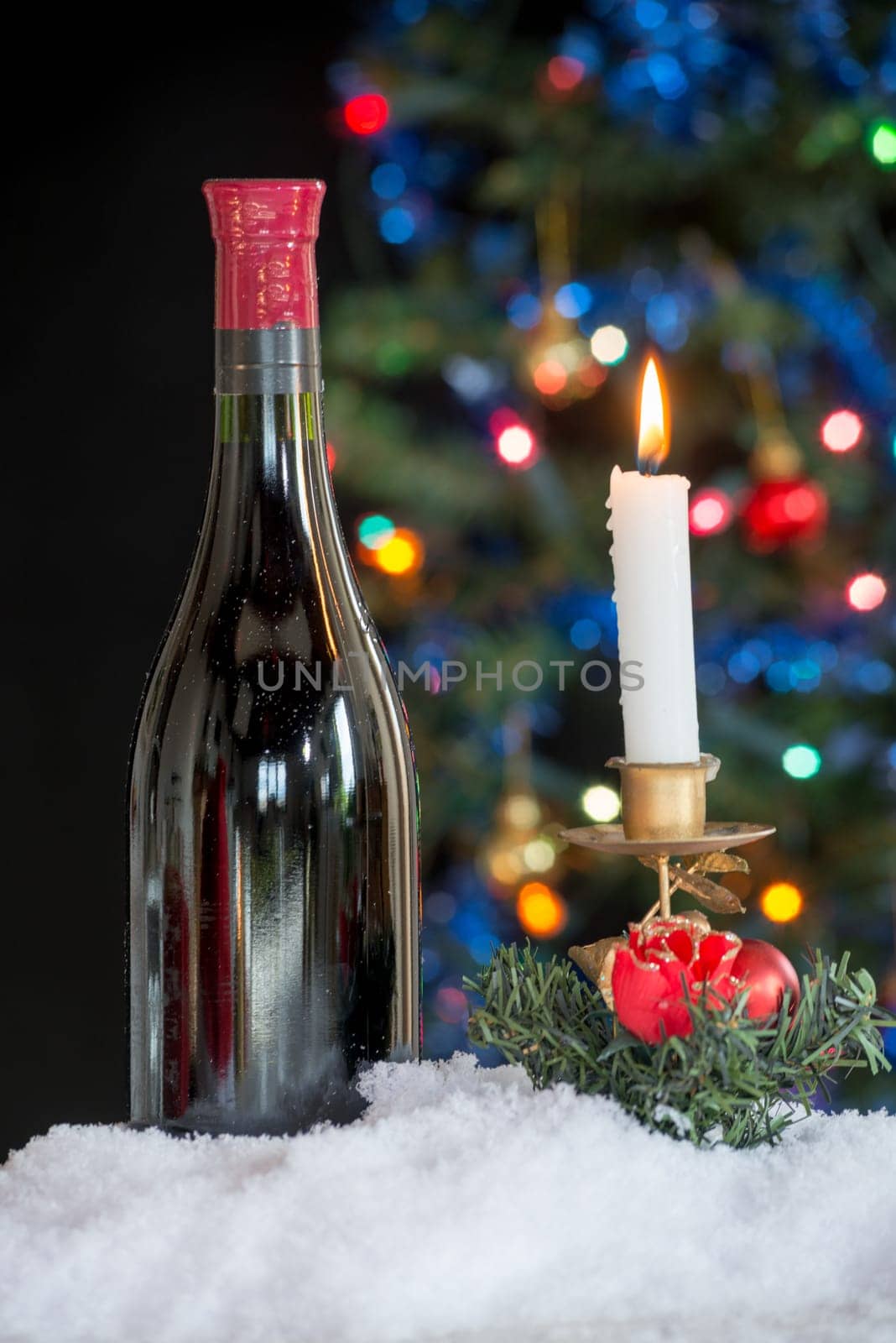 a bottle of red wine and a candle with a Christmas tree in background