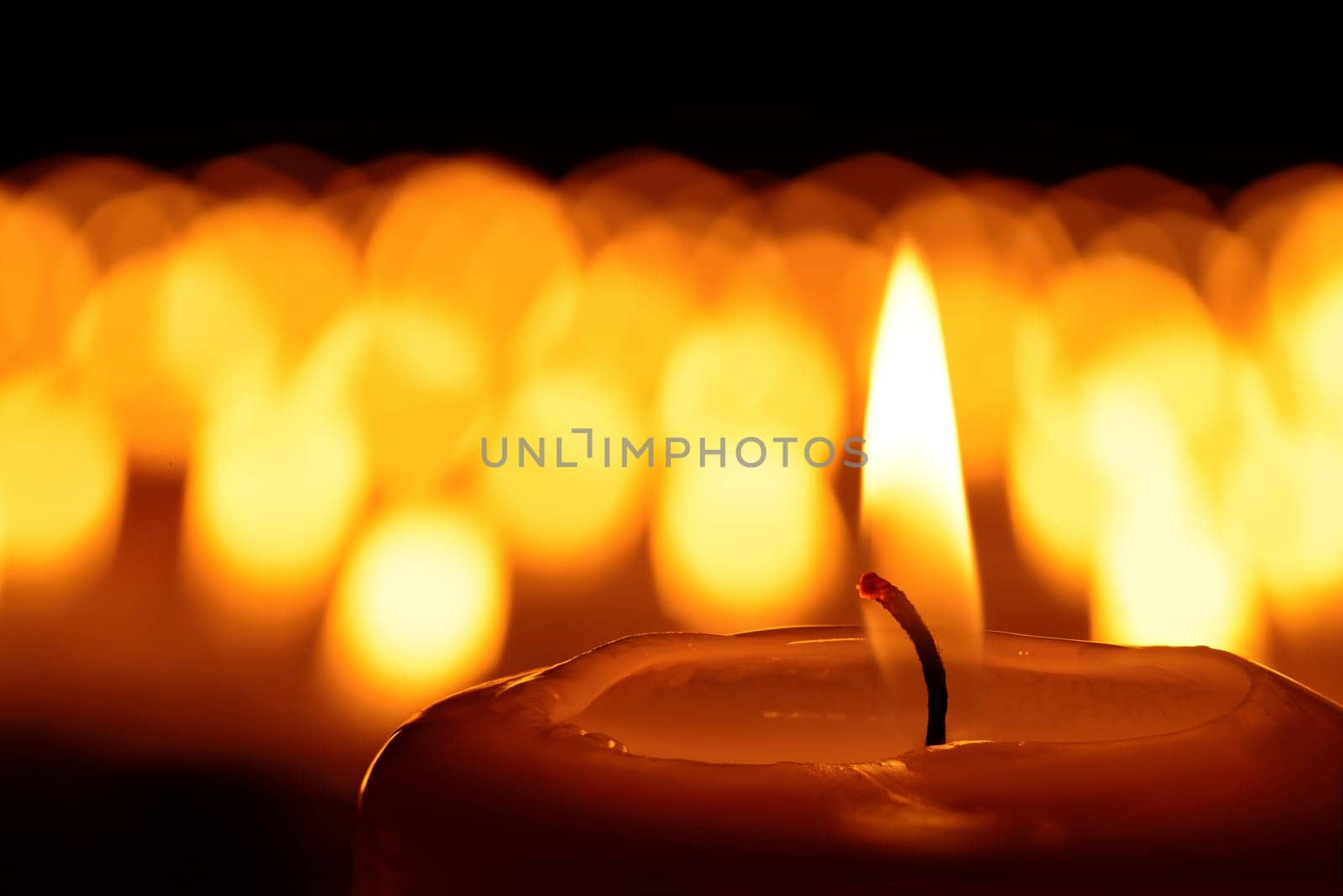 Candle in front of many defocused candleflames creating a spiritual atmosphere and in remembrance of the victims of terror and violence