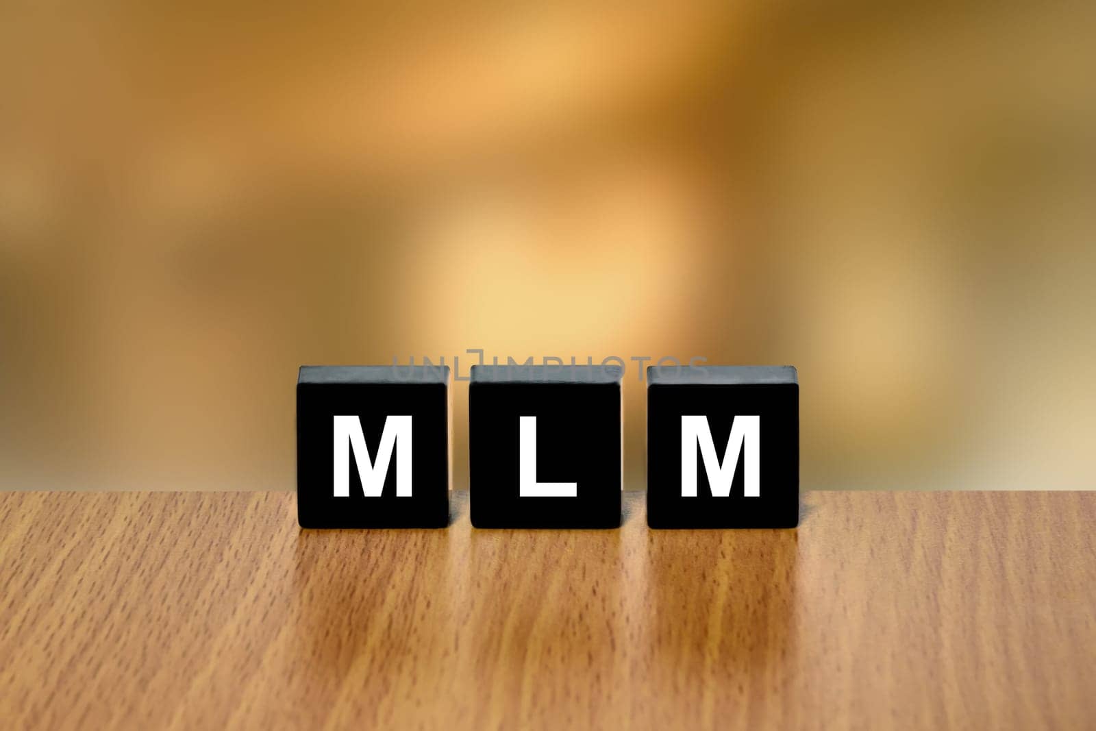 MLM or Multi Level Marketing on black block with blurred background