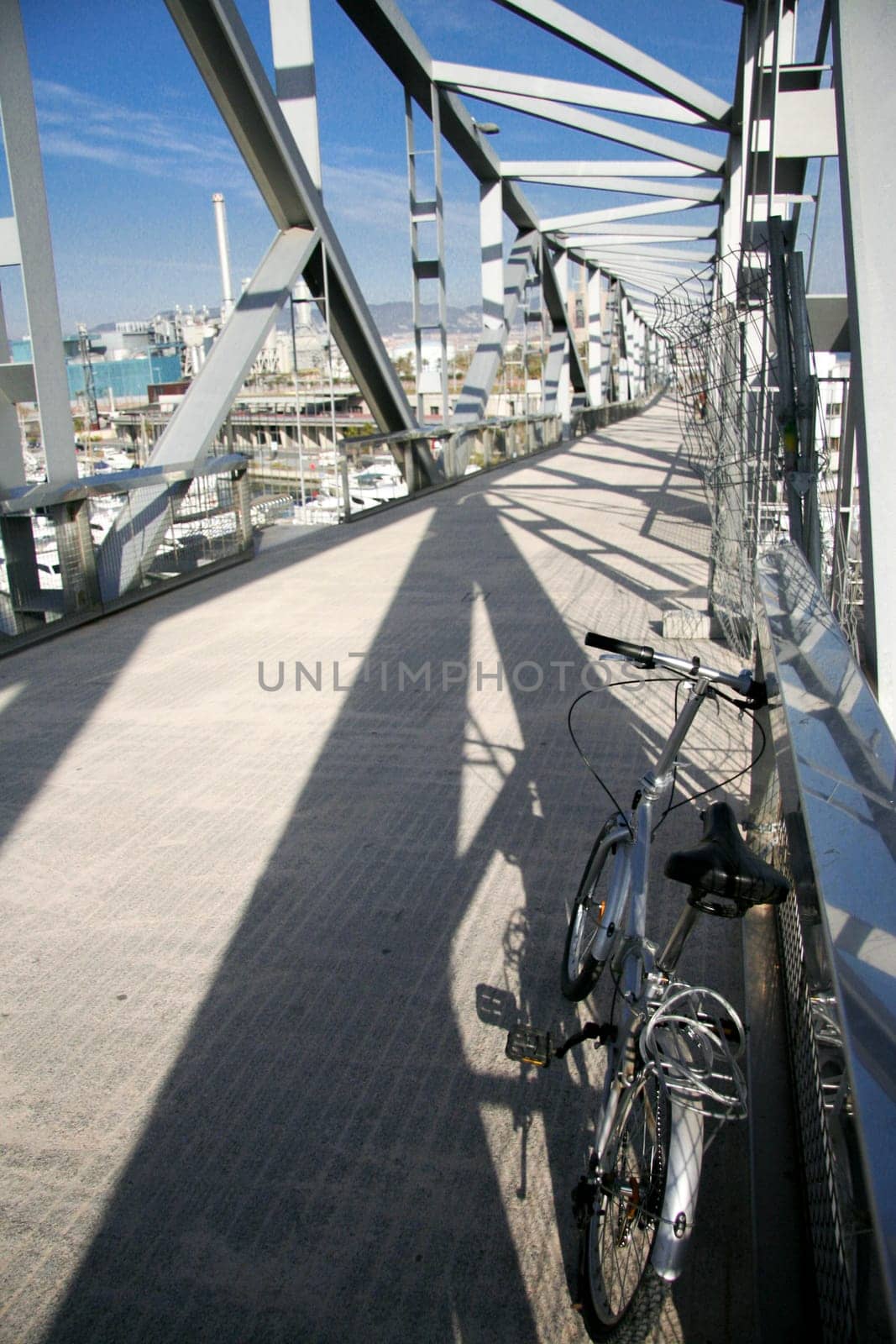 Folding Bike parked over pedestrian truss bridge leads above the marina Port forum in Barcelona