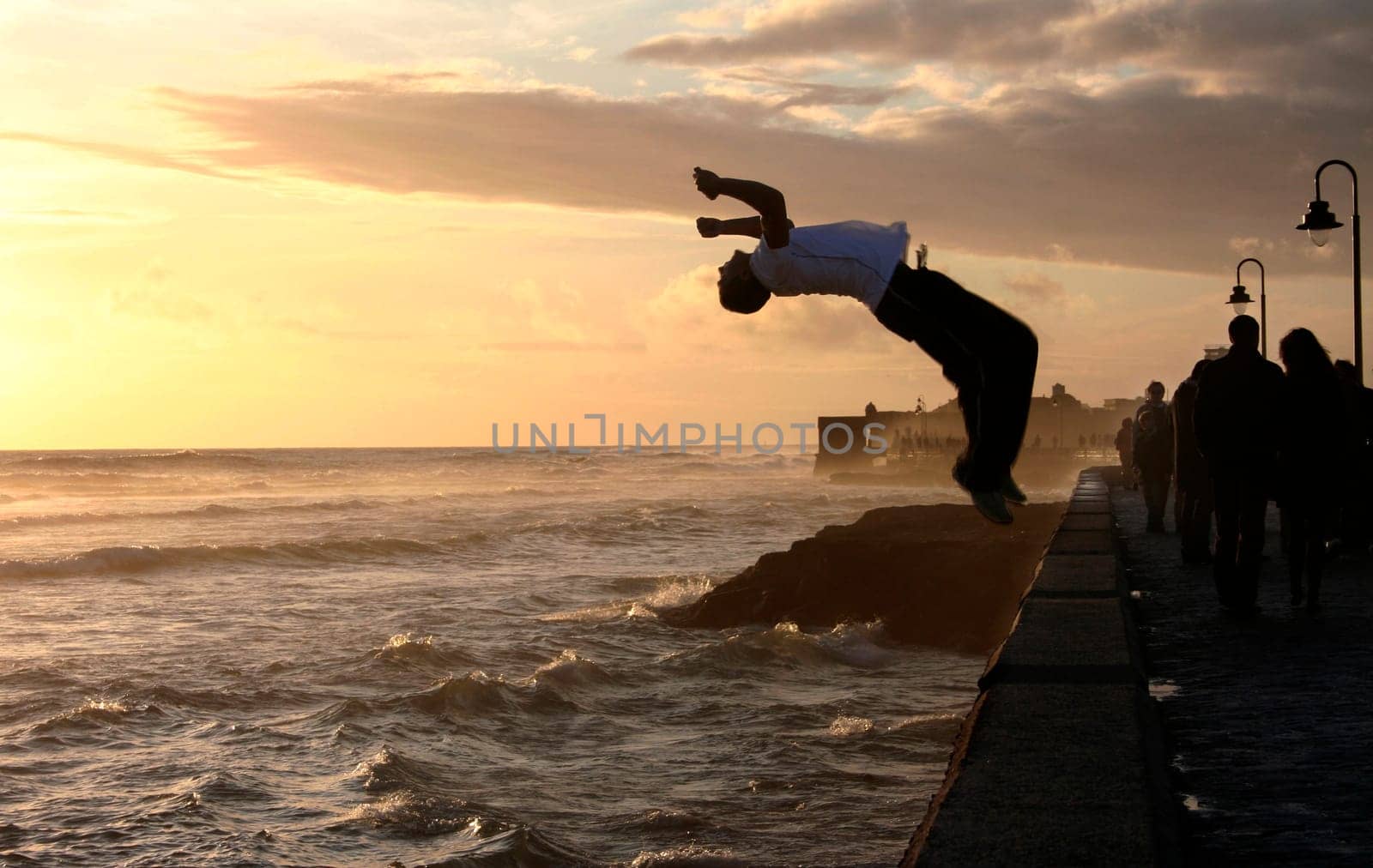 Parkour performer jumping while people walk along the stony boardwalk of Cadiz, Spain