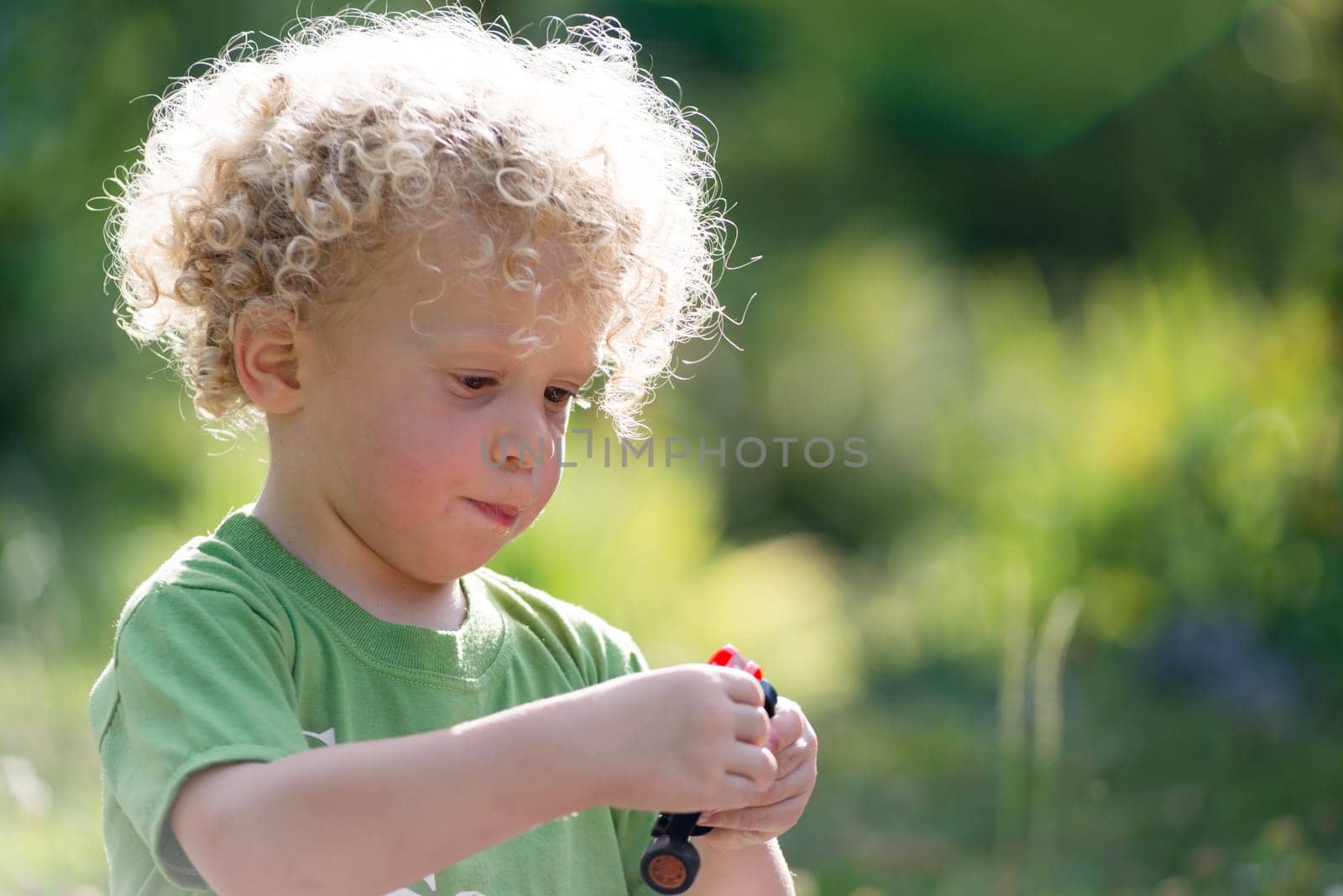 a small blond and curly boy playing with toy car