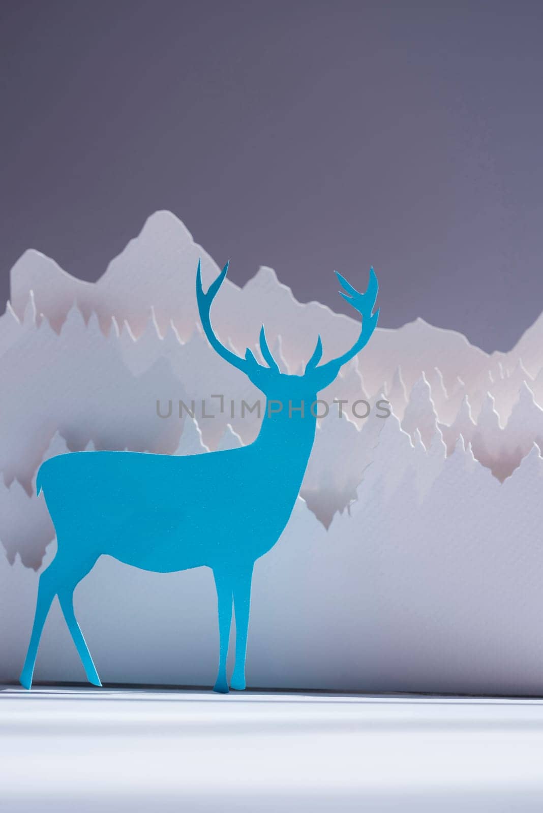 Handmade paper cut deer in blue color with snow forest background. Ideal for holiday greeting card, christmas, new year or campaign.