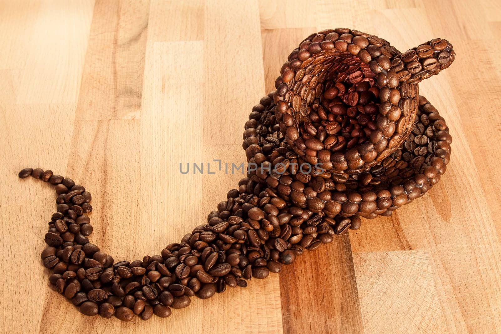 Close up view of a cup covered with coffee beans above a floor covered with coffee beans
