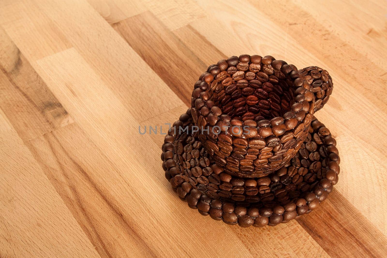 Close up view of a cup covered with coffee beans above a floor covered with coffee beans