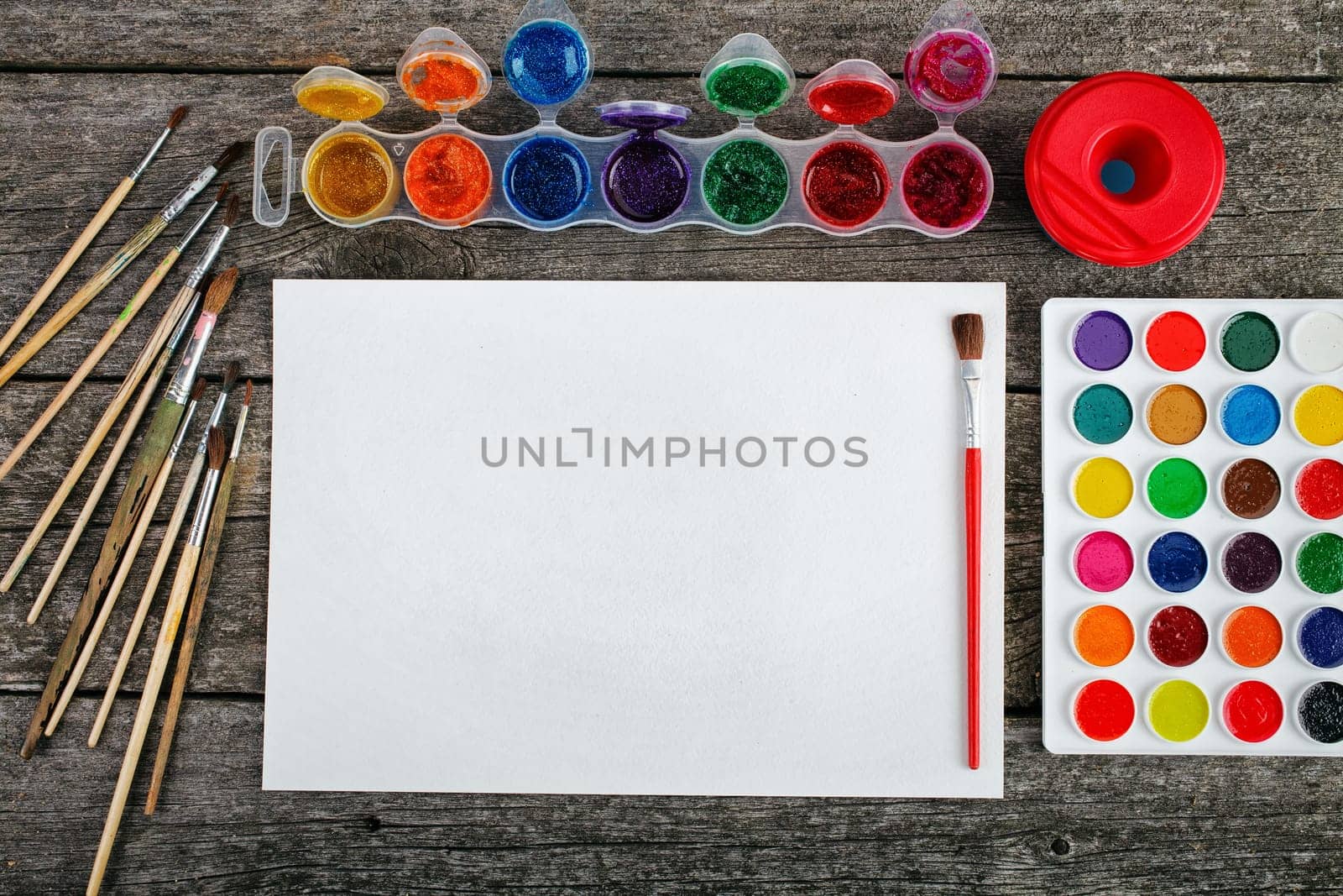 Set of watercolor paints,  brushes for painting and blank white paper sheet of sketchbook on vintage wooden background. Top view.