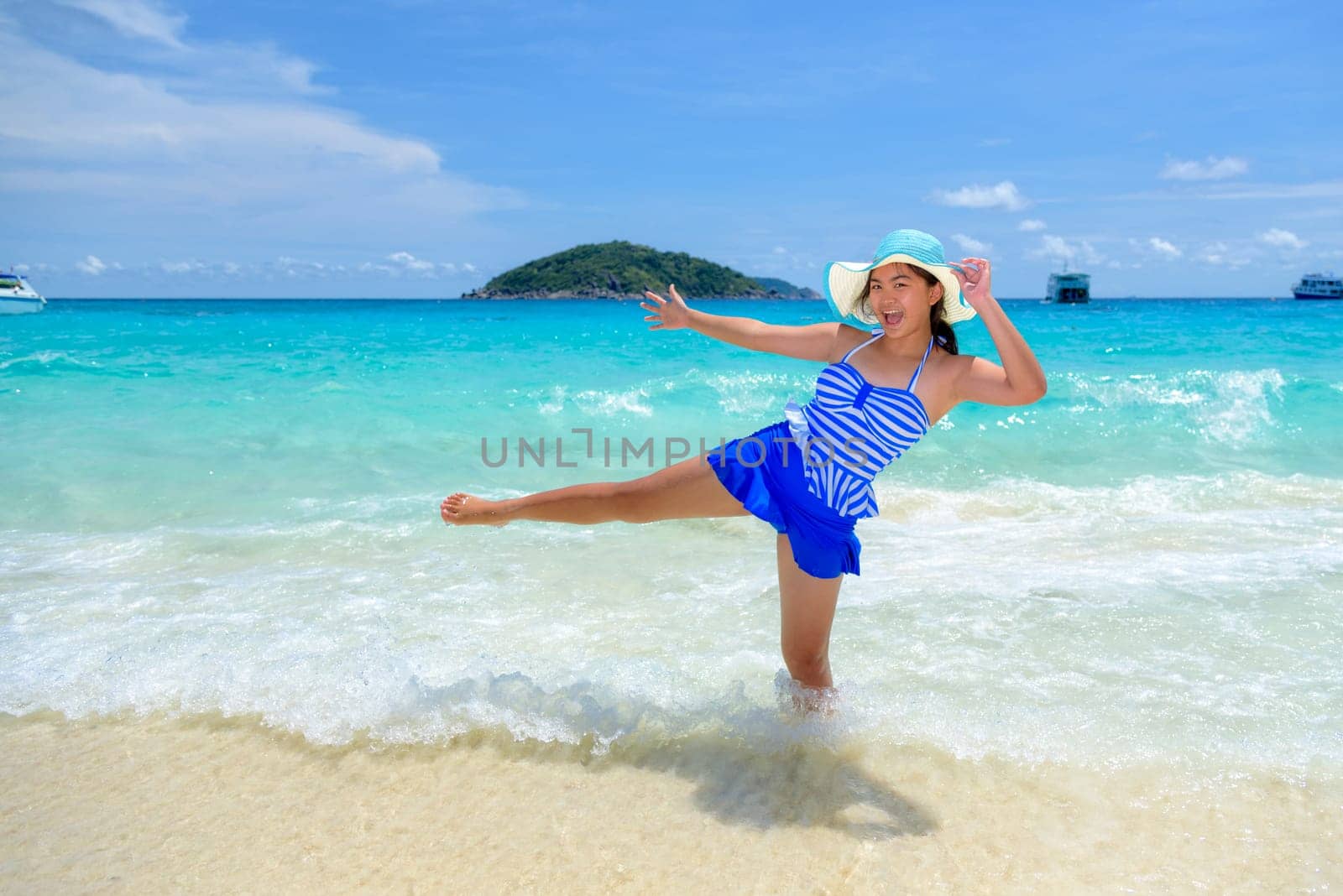 Beautiful woman in a blue white striped swimsuit standing with gestures have fun and happy under summer sky on the beach of Koh Miang Island in Mu Ko Similan National Park, Phang Nga, Thailand