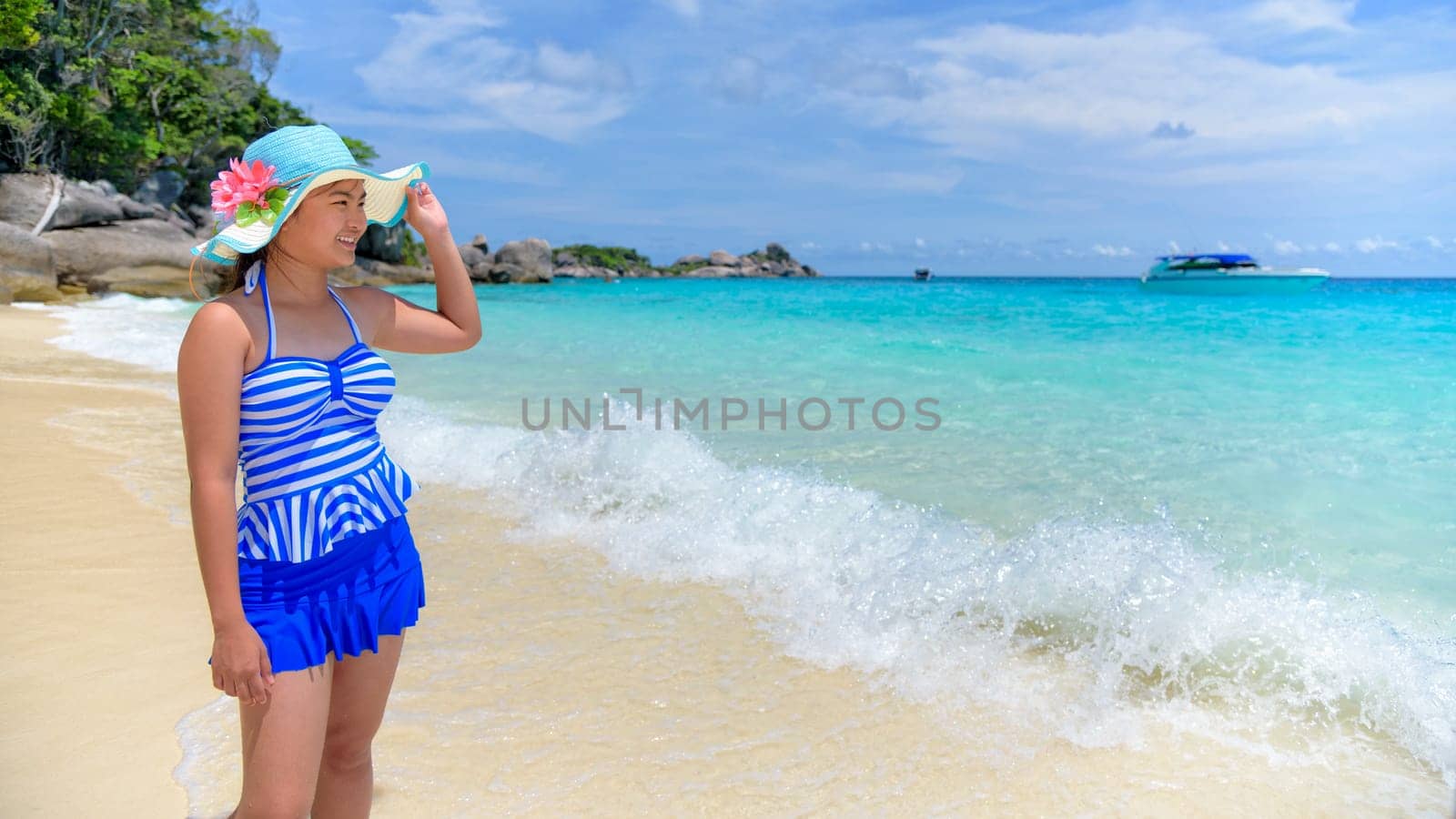 Beautiful woman in a blue striped swimsuit and hat standing poses on beach of sea under a summer sky at Koh Miang Island in Mu Ko Similan National Park, Phang Nga, Thailand, 16