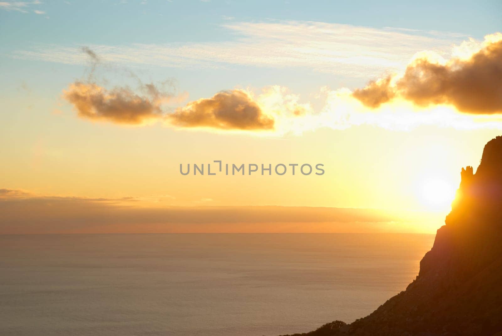 Sunset above the sea with red sky, sun, clouds and mountain