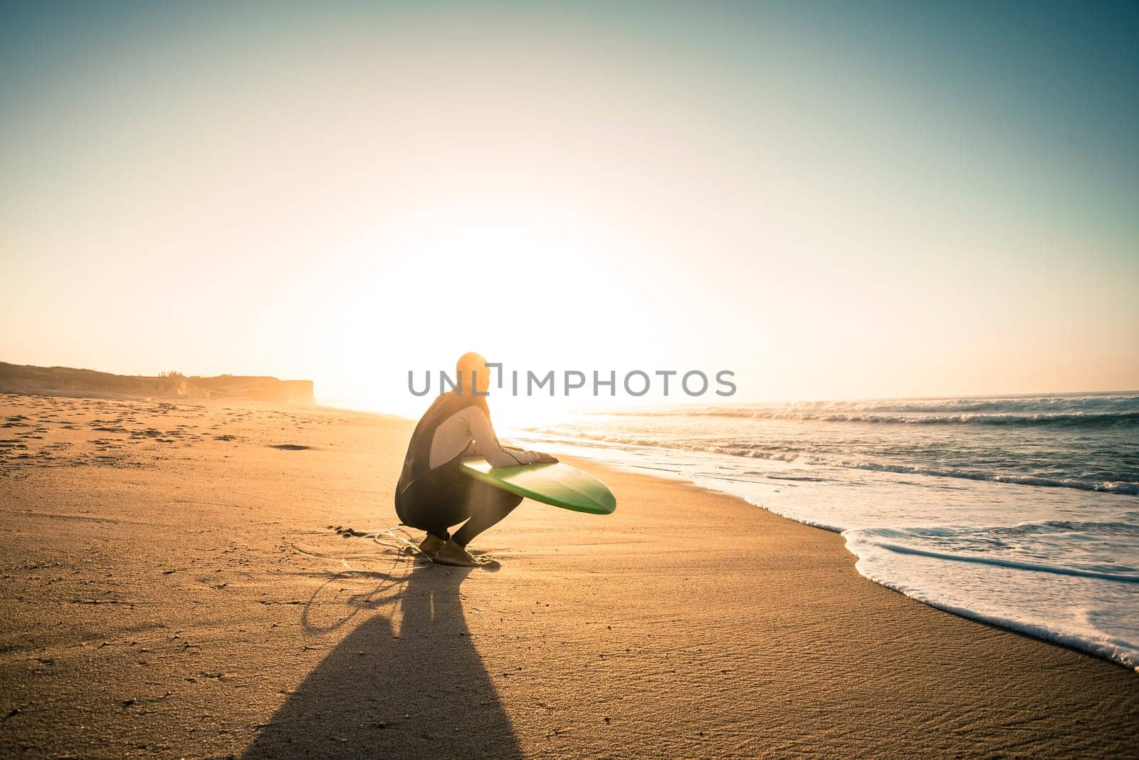 Surfer on the beach holding is surfboaerd and watching the waves
