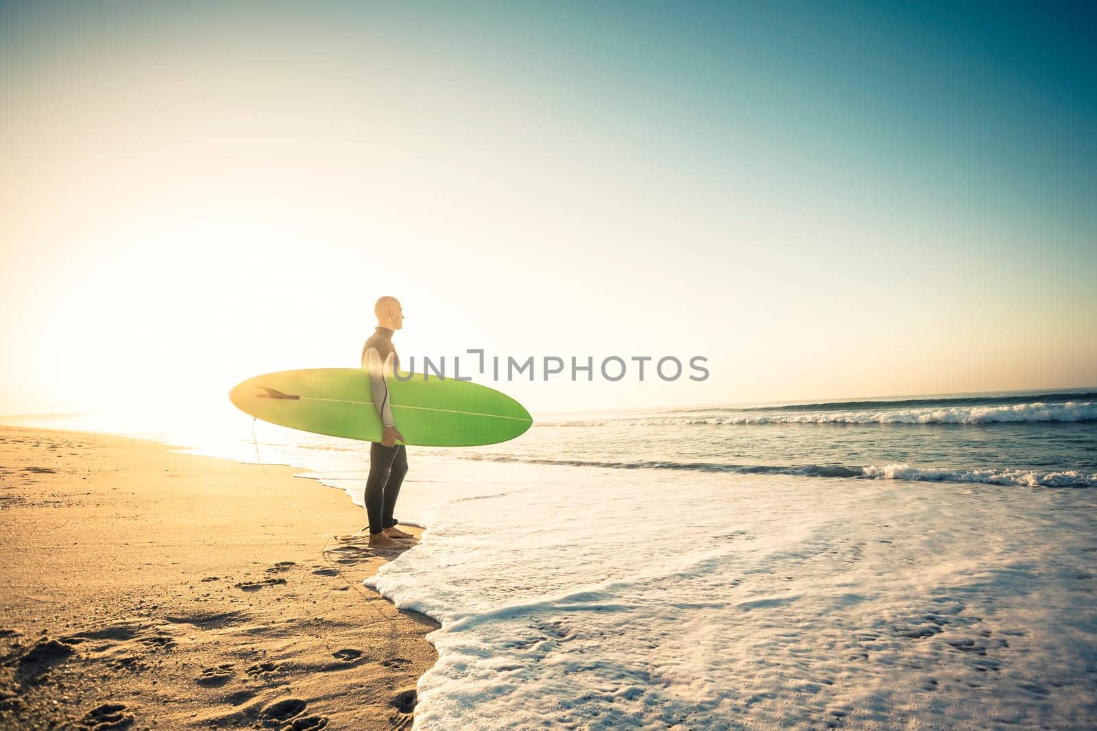 Surfer on the beach holding is surfboaerd and watching the waves