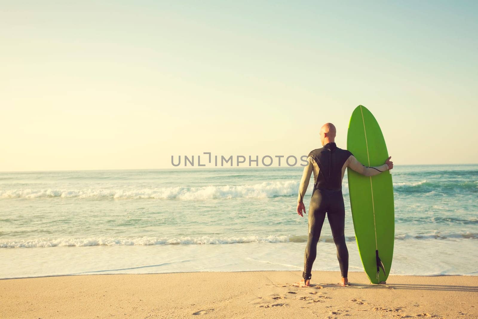 Surfer on the beach holding is surfboaerd and watching the waves