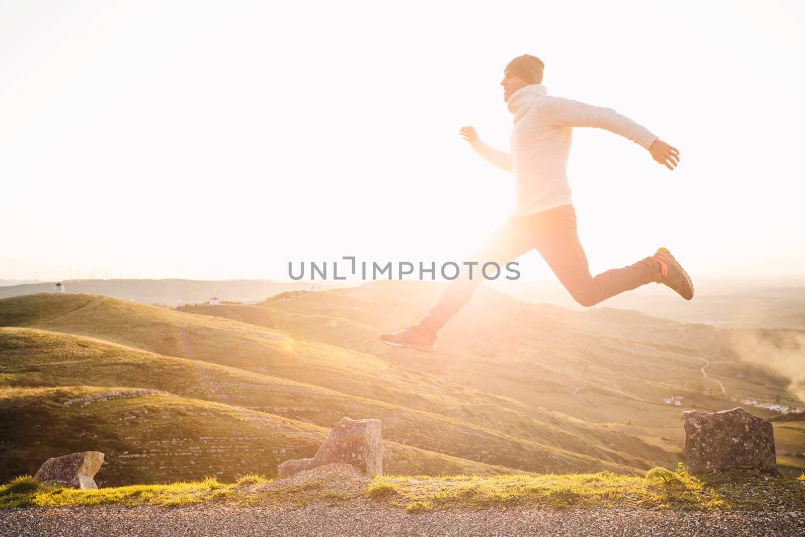 Man jumping over precipice between two stones on mountains at sunset