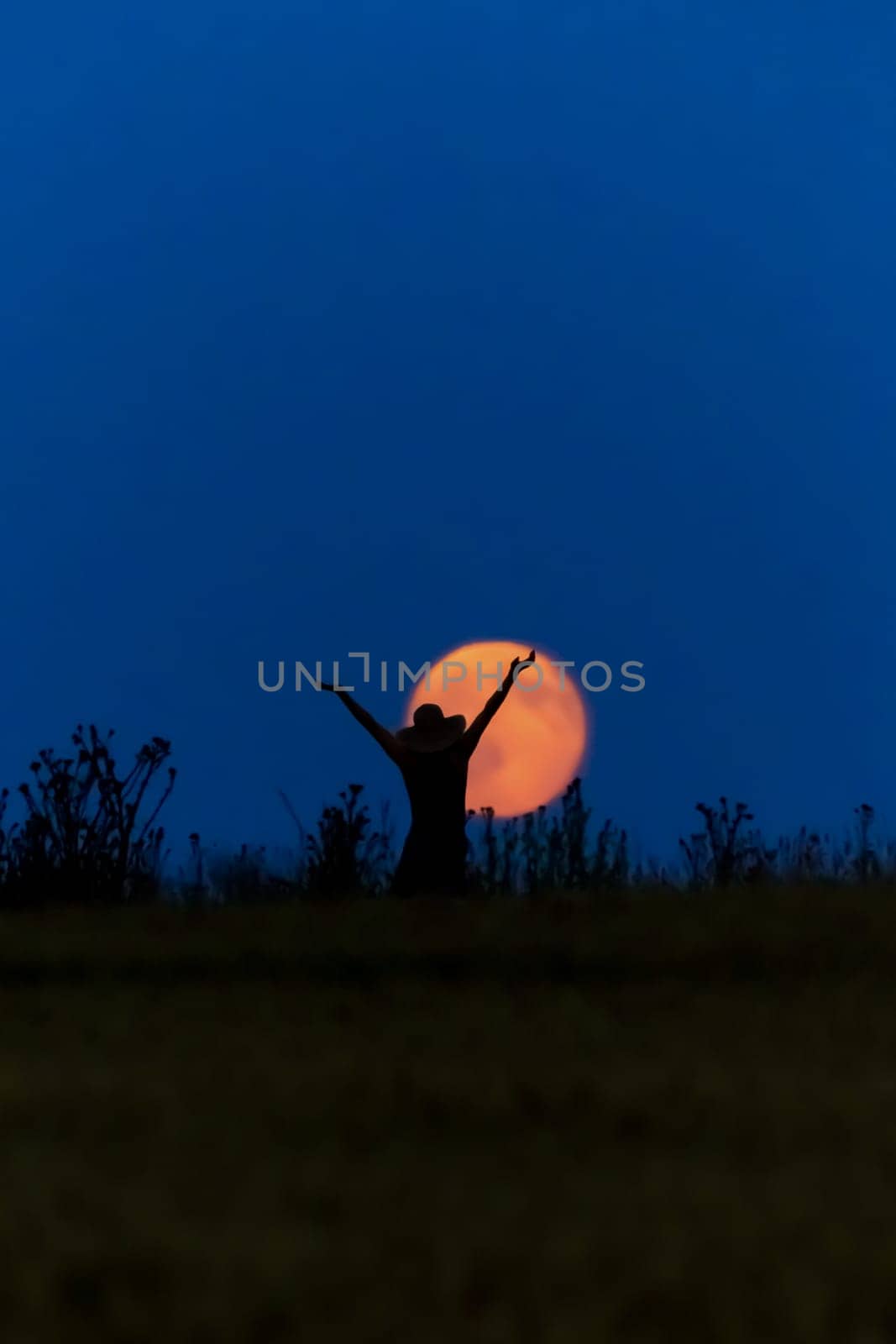 A woman with a hat in front of a full moon is happy
