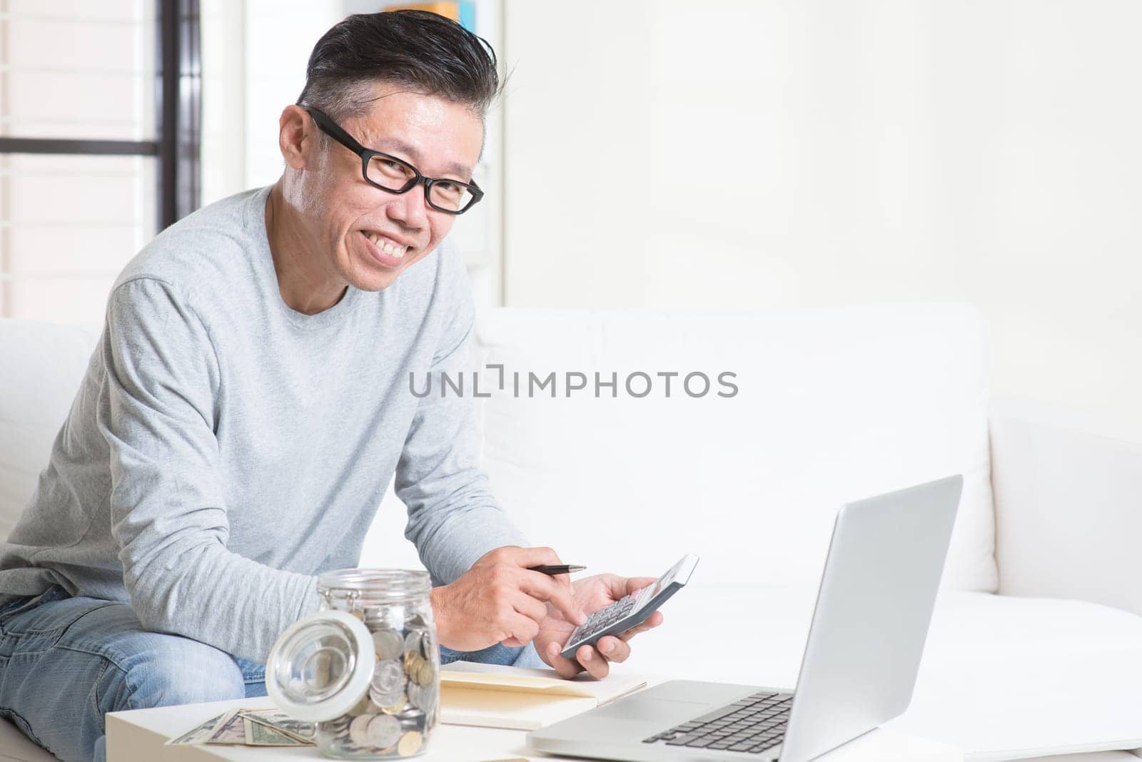 Mature 50s Asian man counting on money using calculator and laptop computer. Saving, retirement, retirees financial planning concept.