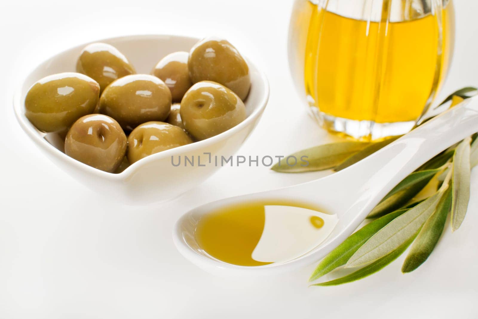 Olive oil in spoon with olives on a white background.